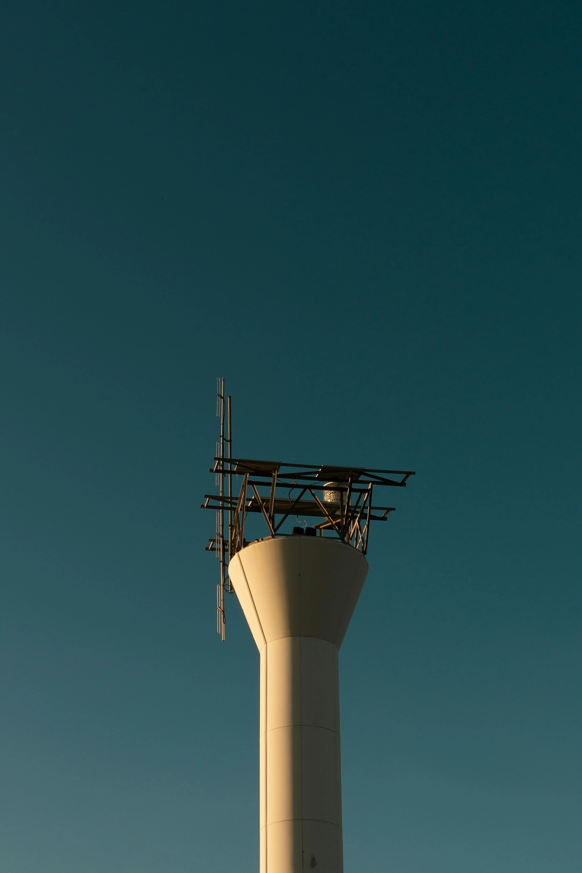 White concrete pillar topped with metal antenna rigging, showcasing distinct styles of radio masts and towers