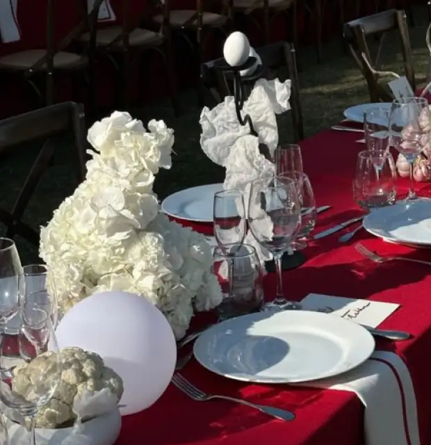 Mesa de evento con mantel rojo, arreglos blancos y vajilla minimalista para proyectos de diseño floral que combinan contraste, textura y elegancia contemporánea.