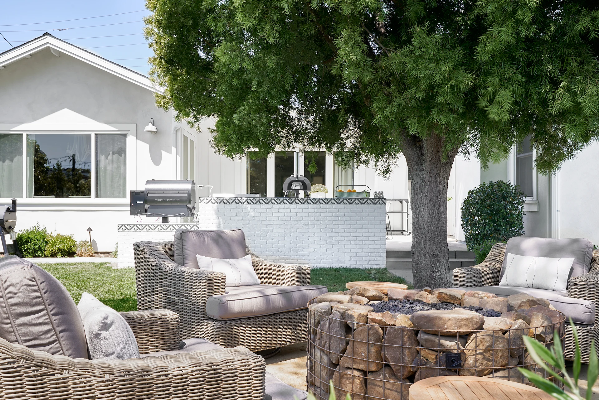 White house with outdoor seating and BBQ setup, surrounded by greenery, in Costa Mesa Exterior Remodel. Photo by Todd Huge.