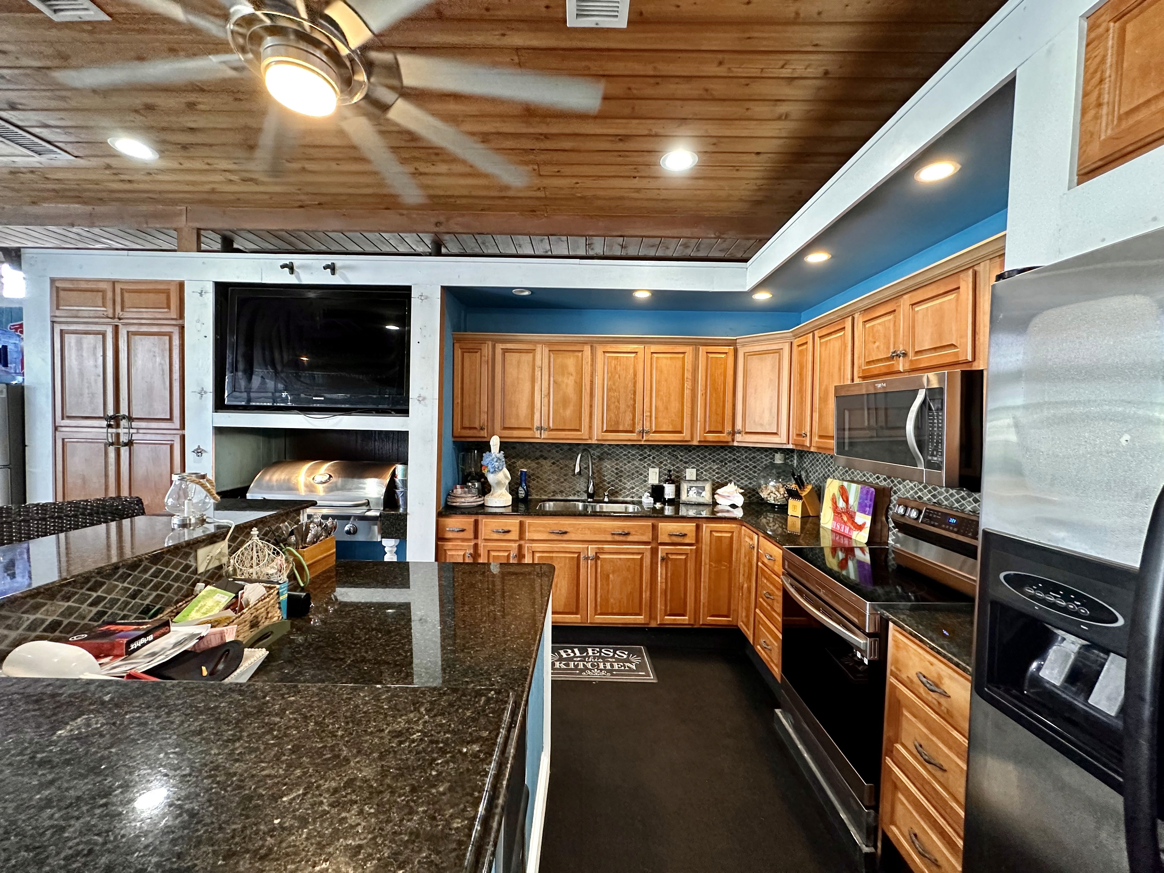 Spacious modern kitchen featuring wooden cabinetry, black granite countertops, stainless steel appliances, and ceiling fan, with a warm, inviting atmosphere and abundant natural light.