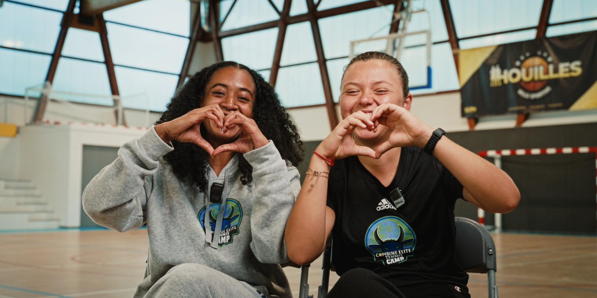 Deux participantes souriantes formant un cœur avec les mains dans un gymnase.