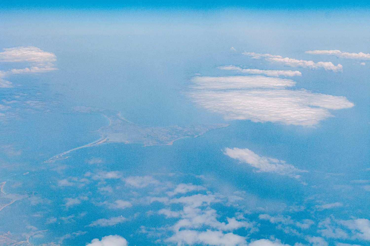 Aerial view above the clouds showing a bright blue sky and distant landforms