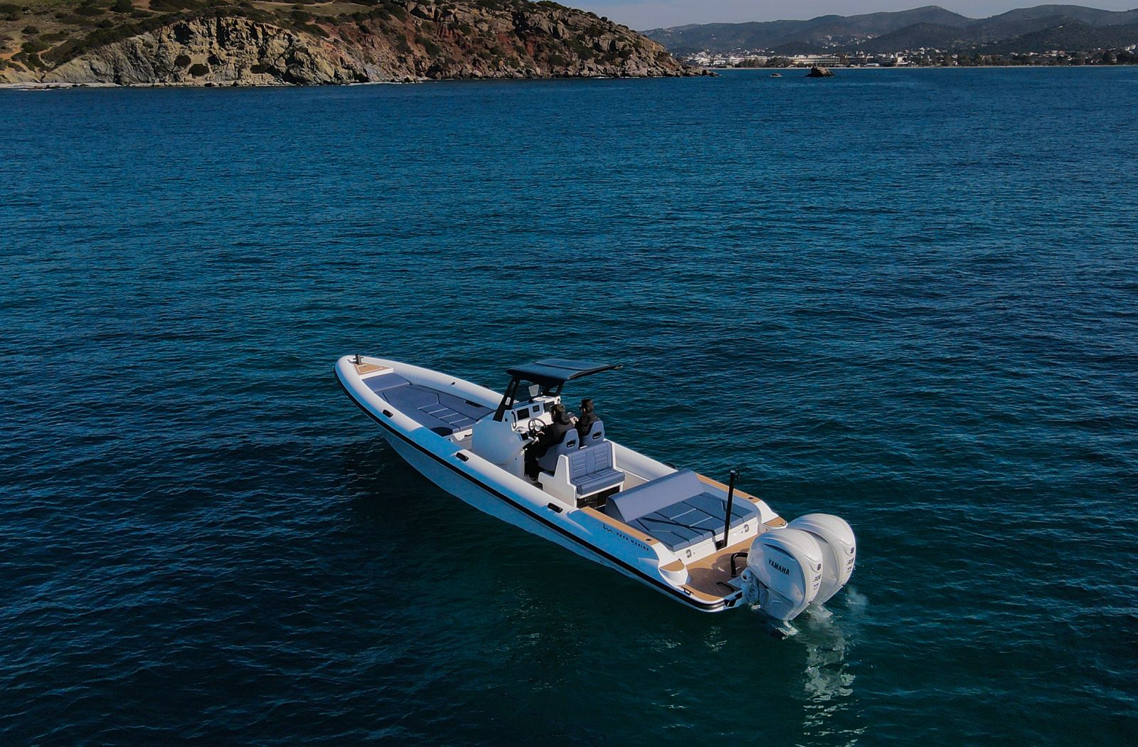 White Rock 36 speedboat with captain at helm cruising calm blue waters near Paros coastline with hills in background.