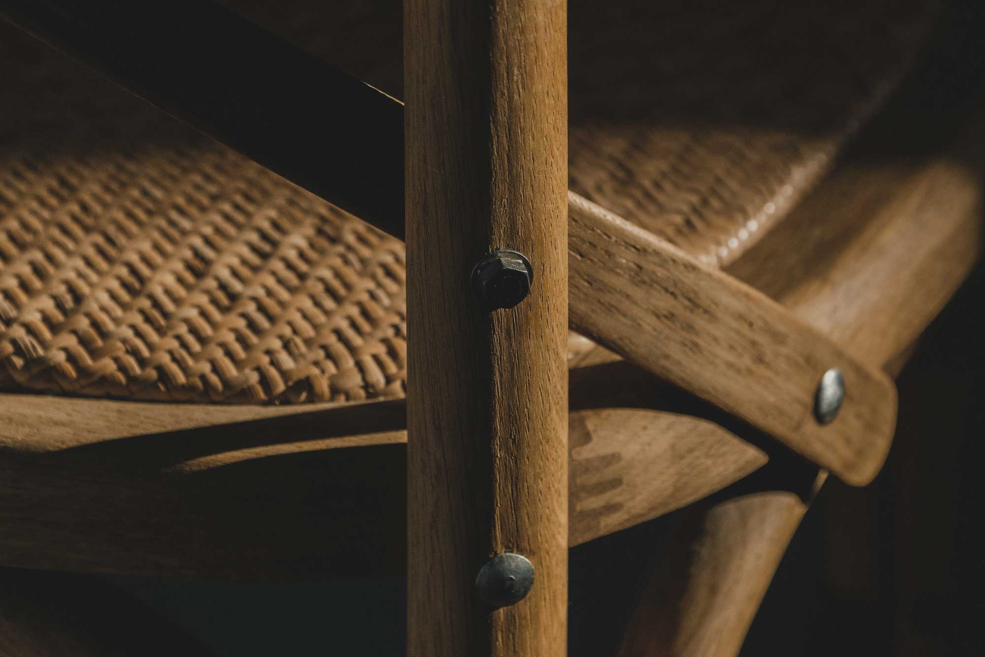 Close-up of a wooden chair showing its woven seat, wooden frame, and metal bolts.