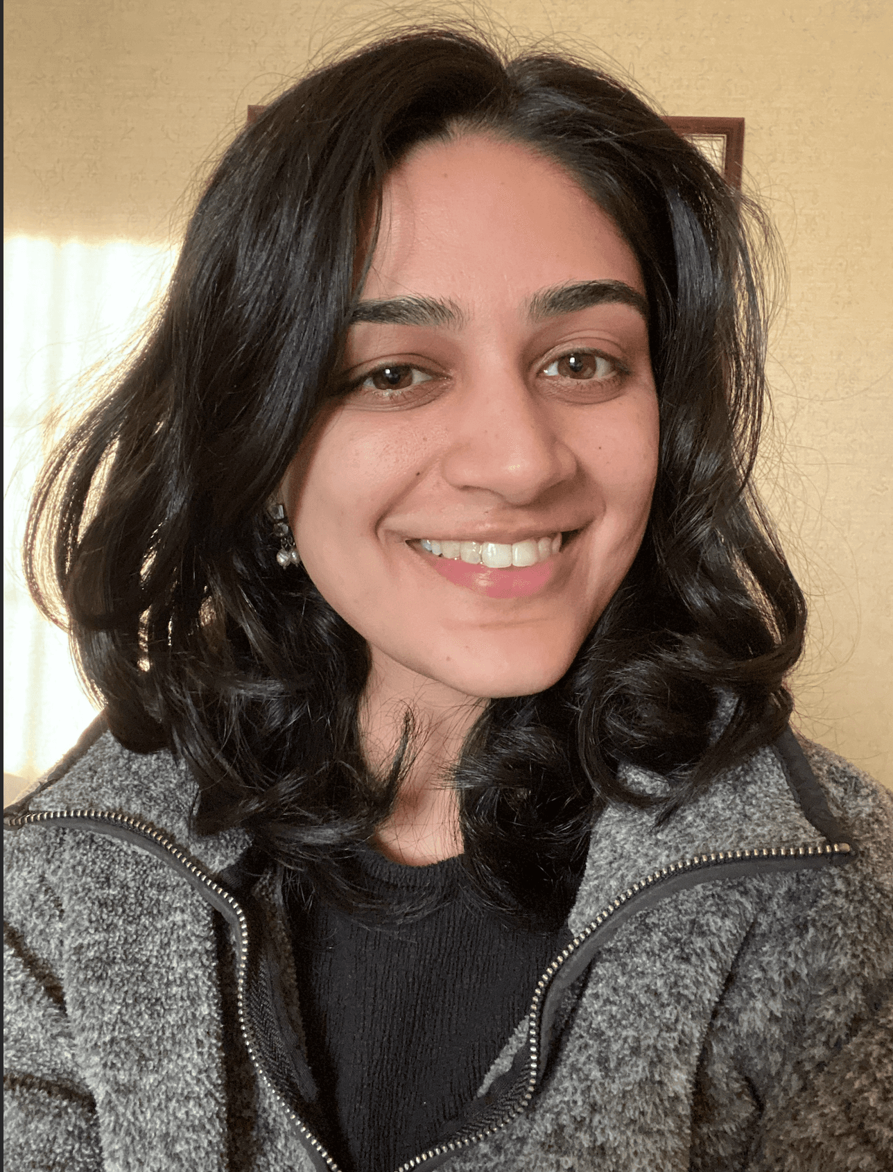 A person stands outdoors in a natural setting with lush green trees under a clear sky, wearing a dark sweatshirt, and looking into the distance.