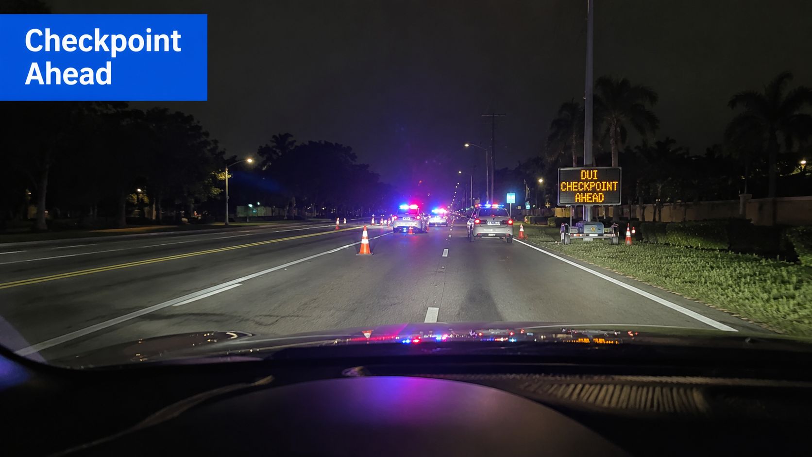A view from inside a car approaching a DUI checkpoint at night with police cars and flashing lights.