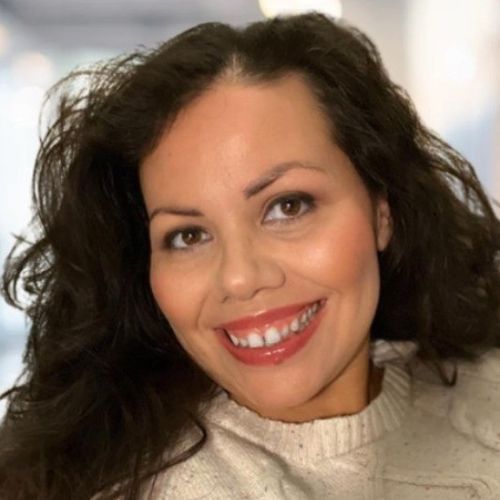 A woman with straight blonde hair wearing a light colored sweater looks away.