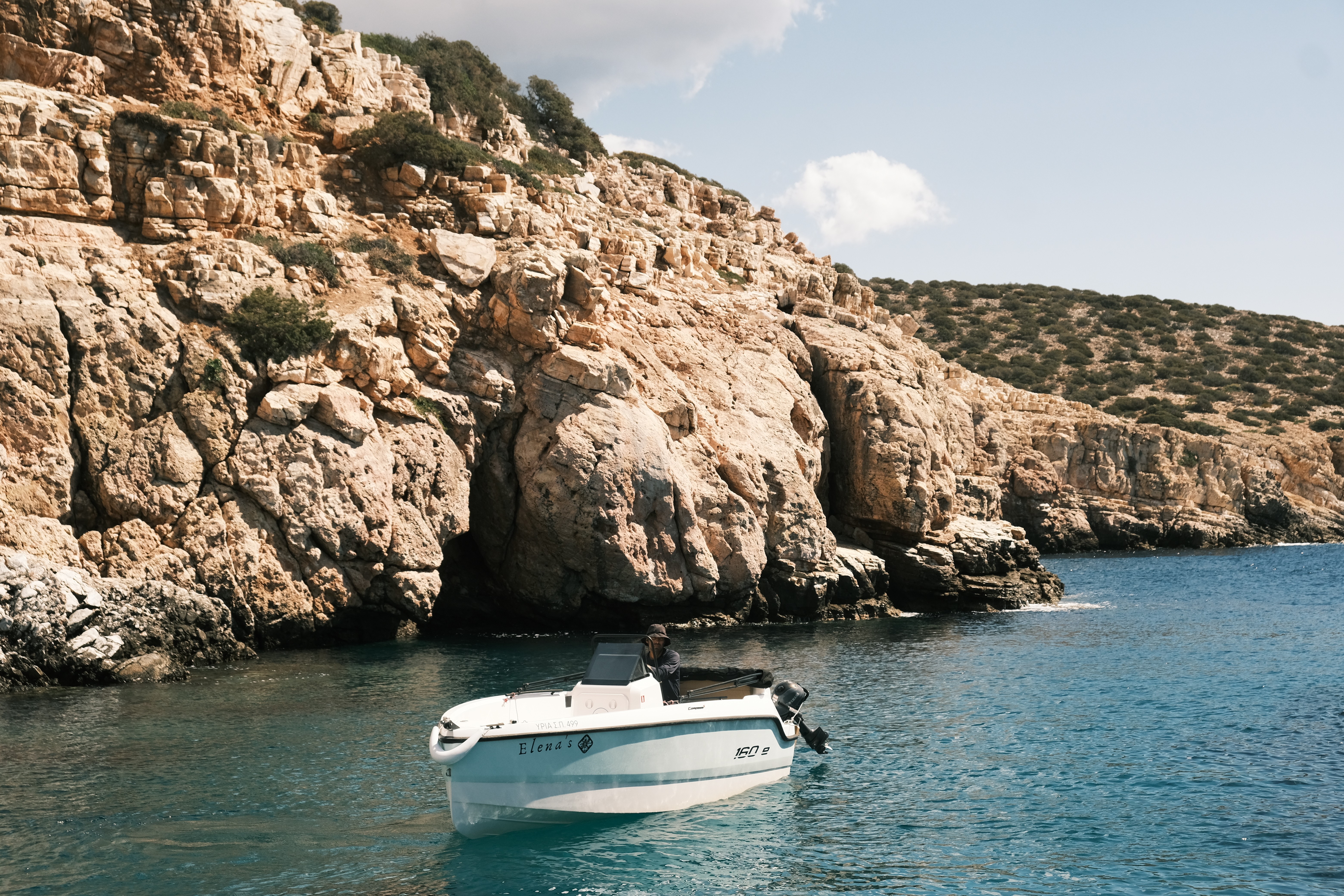 White Compass 16Oe yacht anchored in turquoise waters beside dramatic limestone cliffs with vegetation on top.
