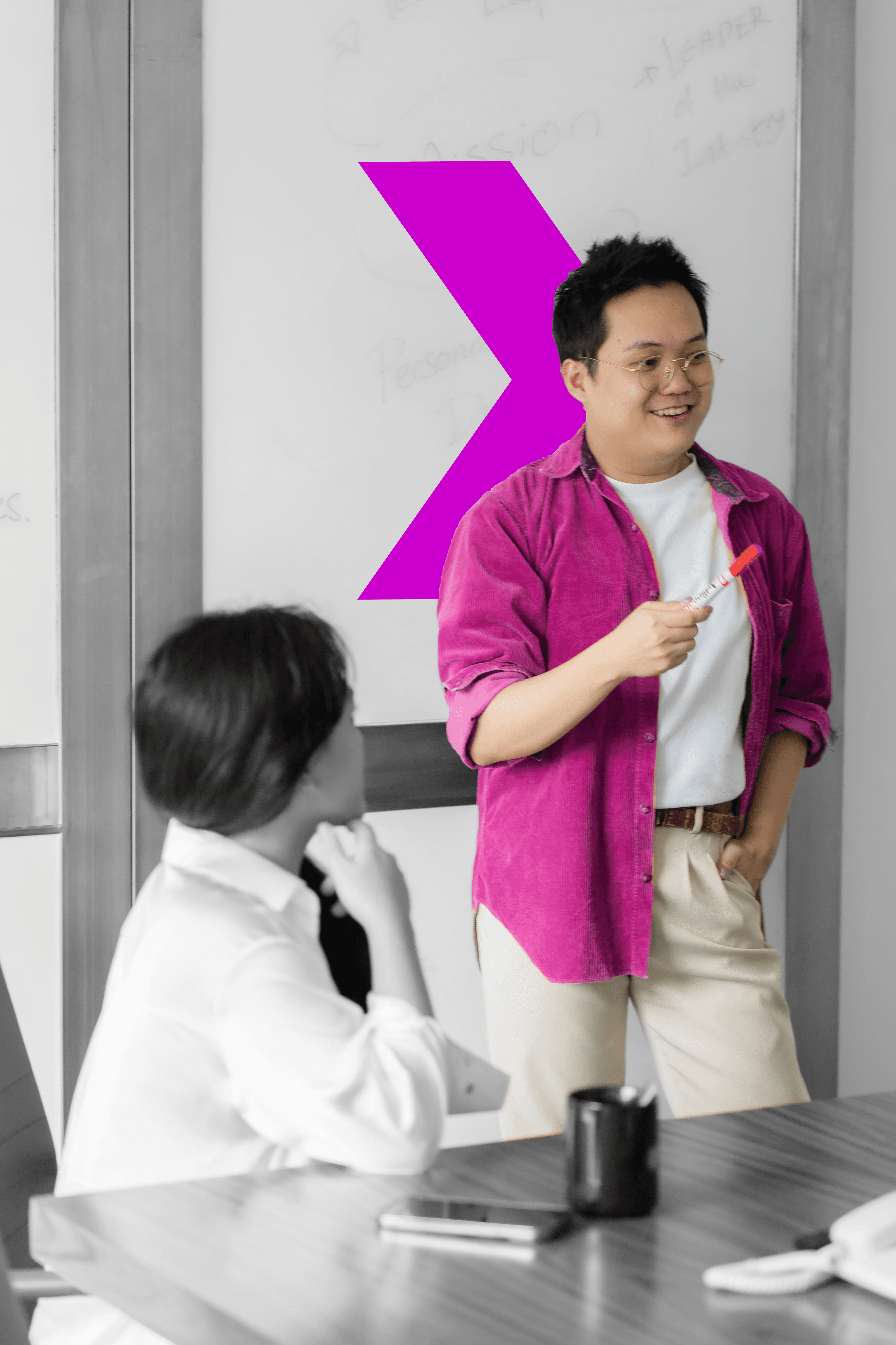 A man and woman discuss ideas in a meeting room, with a vibrant pink arrow pointing towards a goal on the wall.