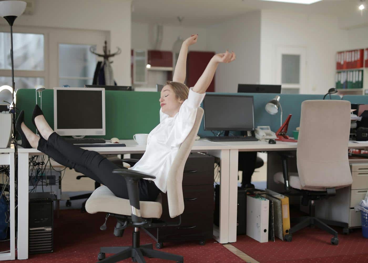 Woman sitting with legs crossed on top of desk and stretching arms above her head