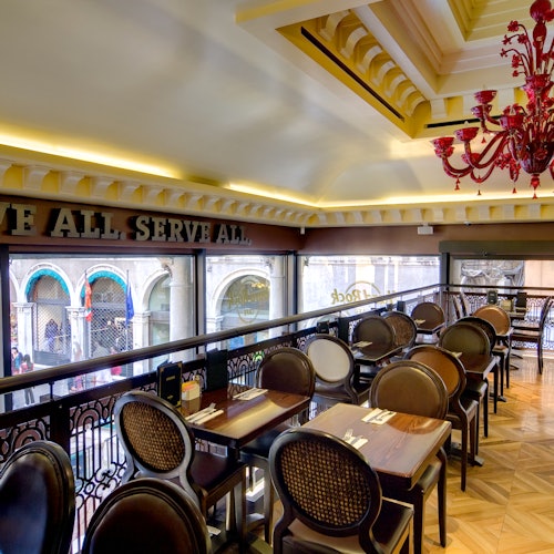 现代室内用餐区，配有棕色座椅、木质餐桌、红色吊灯，以及可俯瞰富有建筑特色街景的大面积窗户。