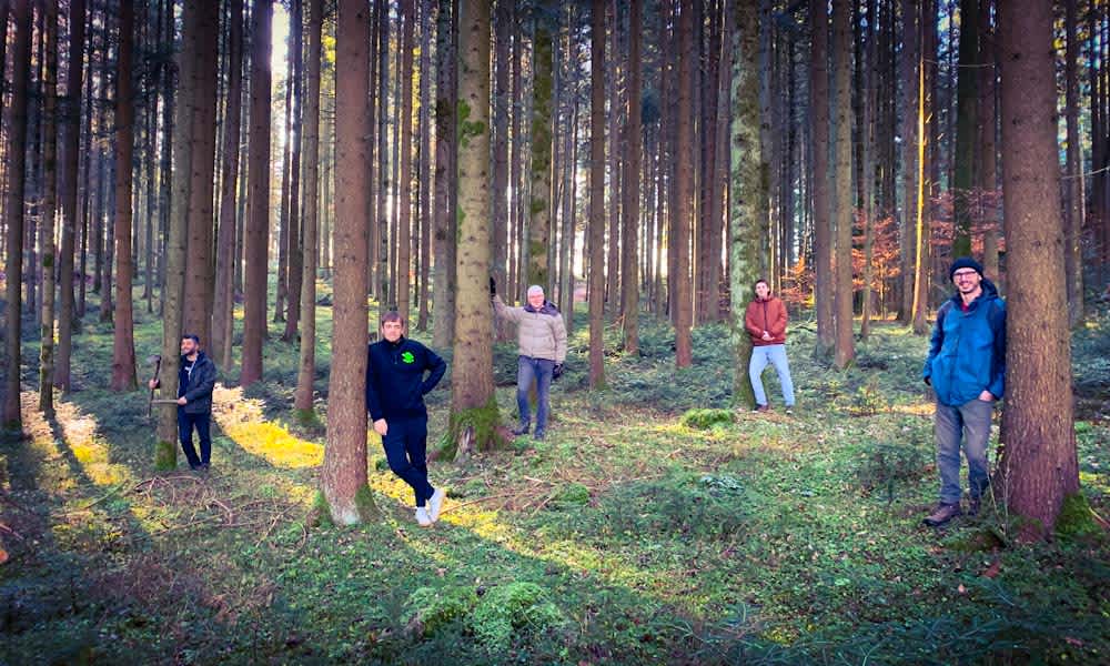 Five people are leaning against trees in the forest.