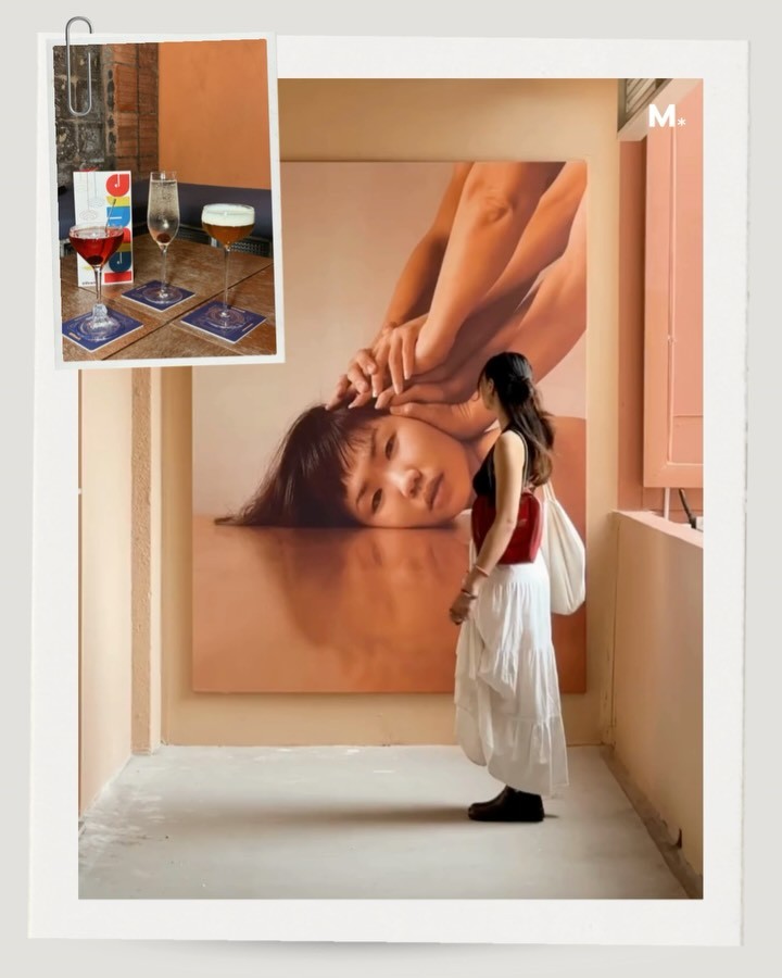 A person standing in front of a large artistic portrait of a woman, set against a warm-toned wall, with a table of drinks and a menu visible in the top corner.