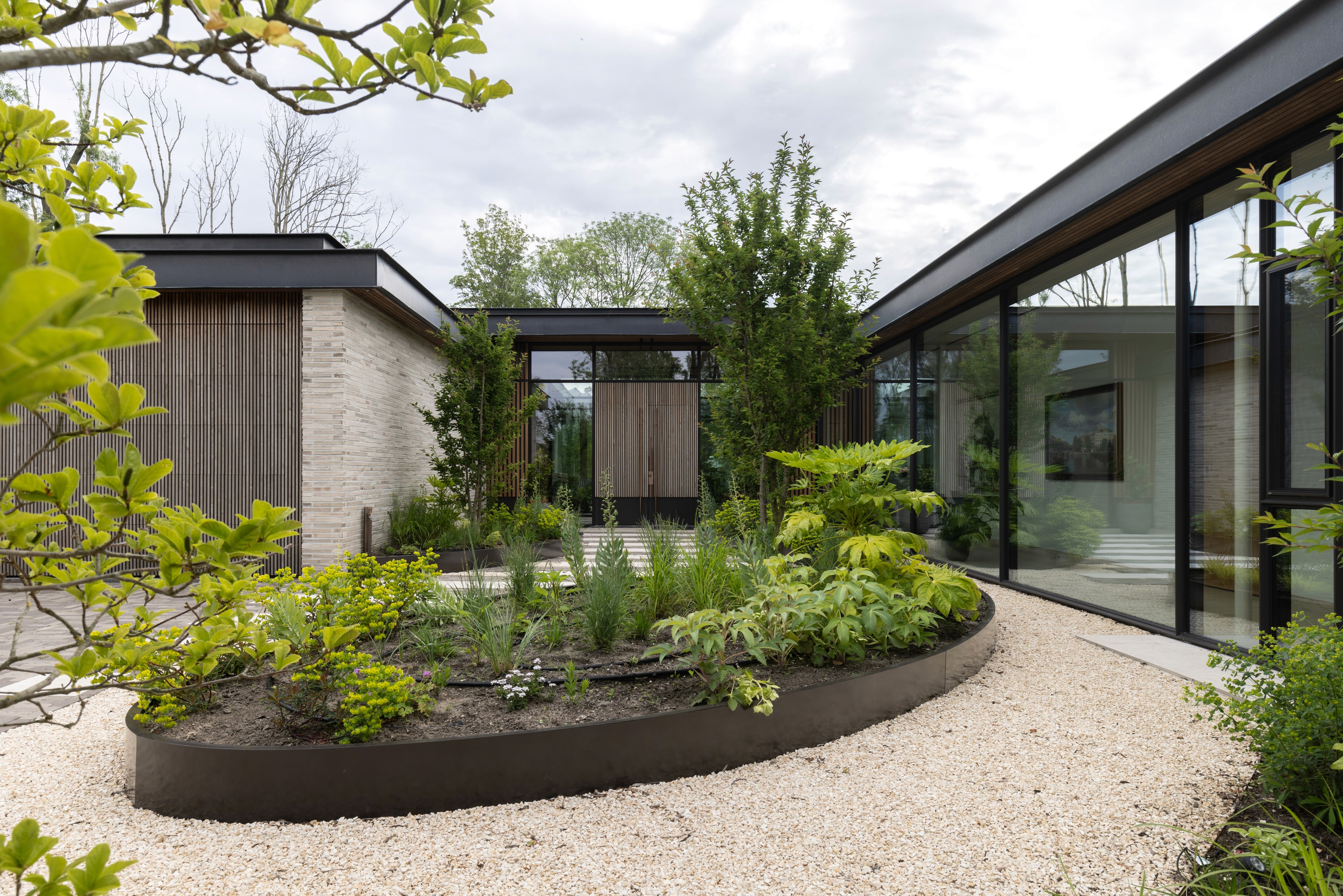 Tuin met moderne architectuur, grindpad, beplanting in metalen bak.