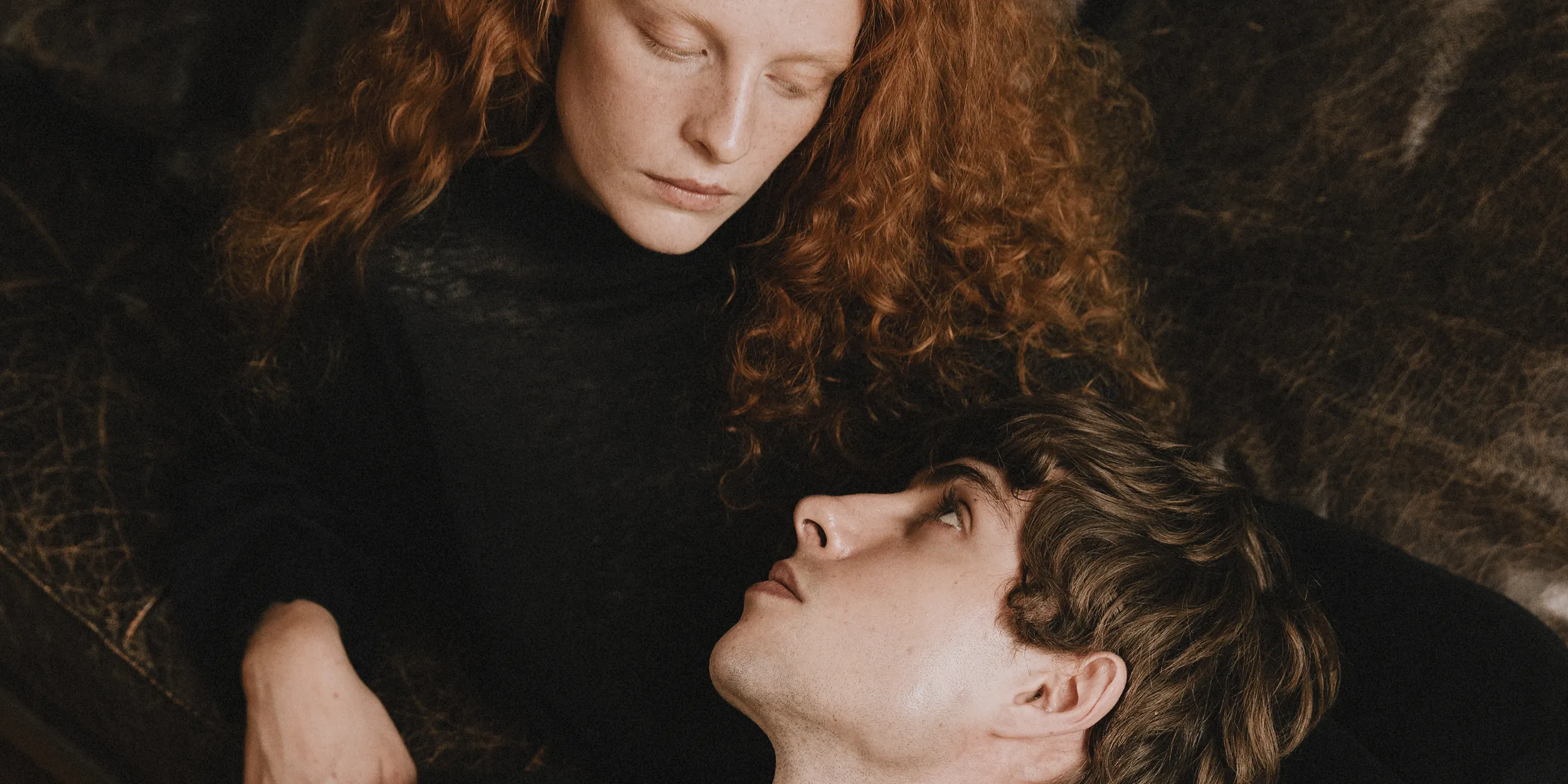 Annapurna SS26 collection campaign image of a couple wearing black sheer knitwear lounging on a rug.