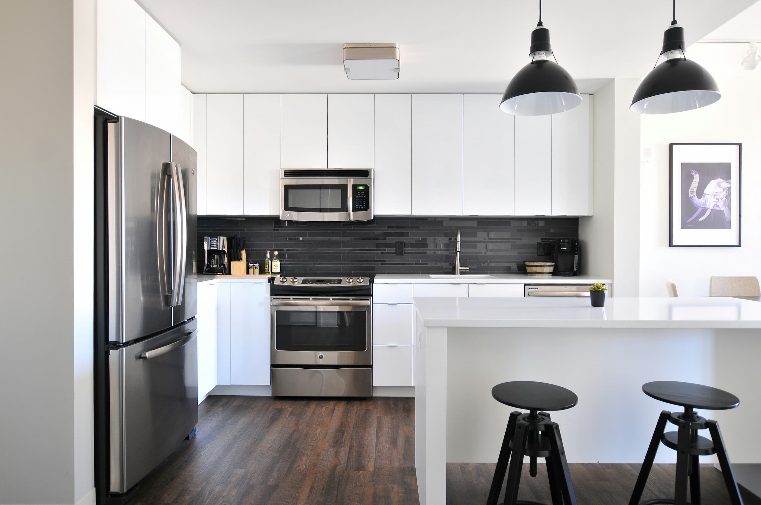 Modern kitchen with white cabinets, stainless steel appliances, and black backsplash in a renovated home.