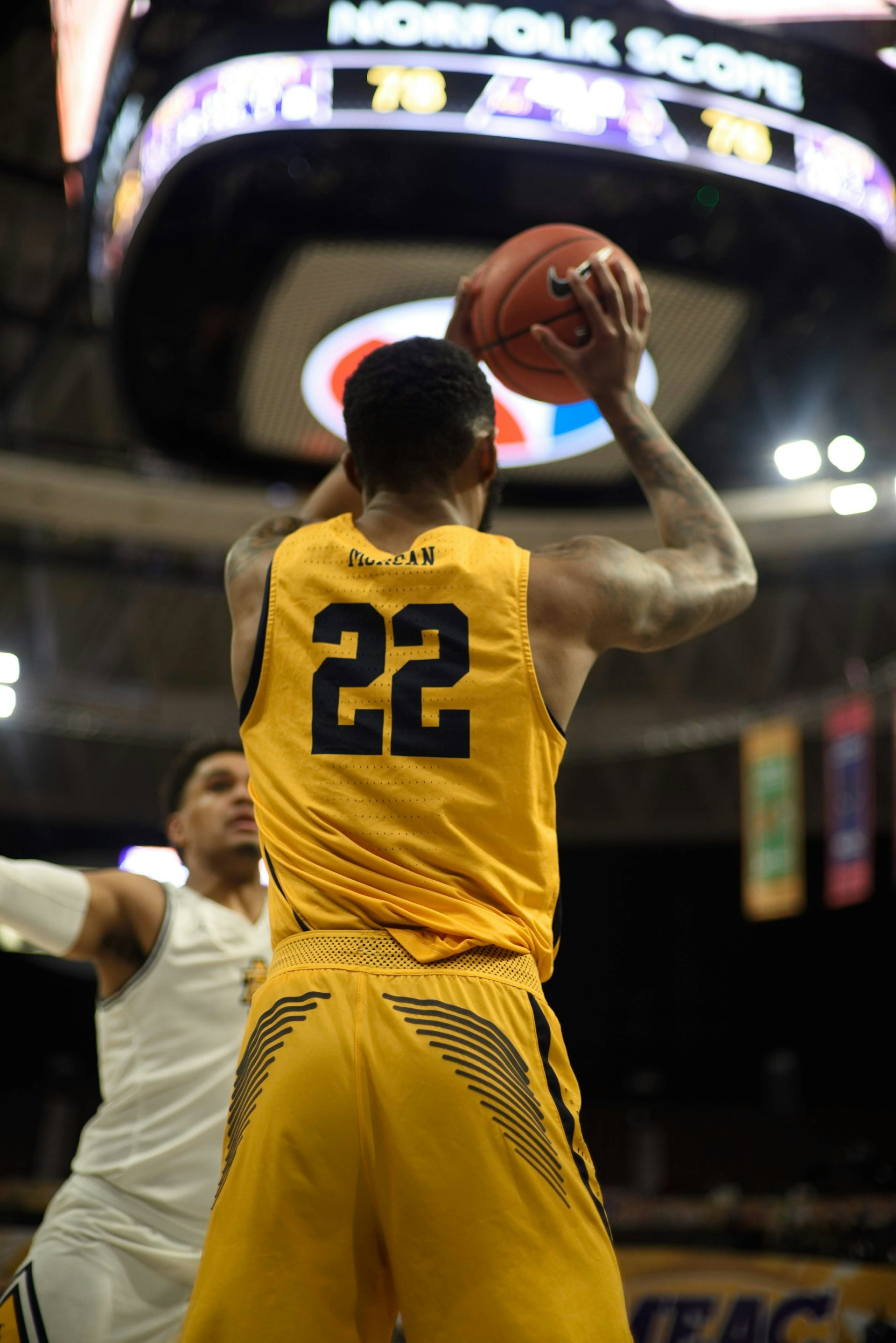 Rear view of a basketball player in a yellow jersey (number 22) taking a jump shot in an indoor arena.