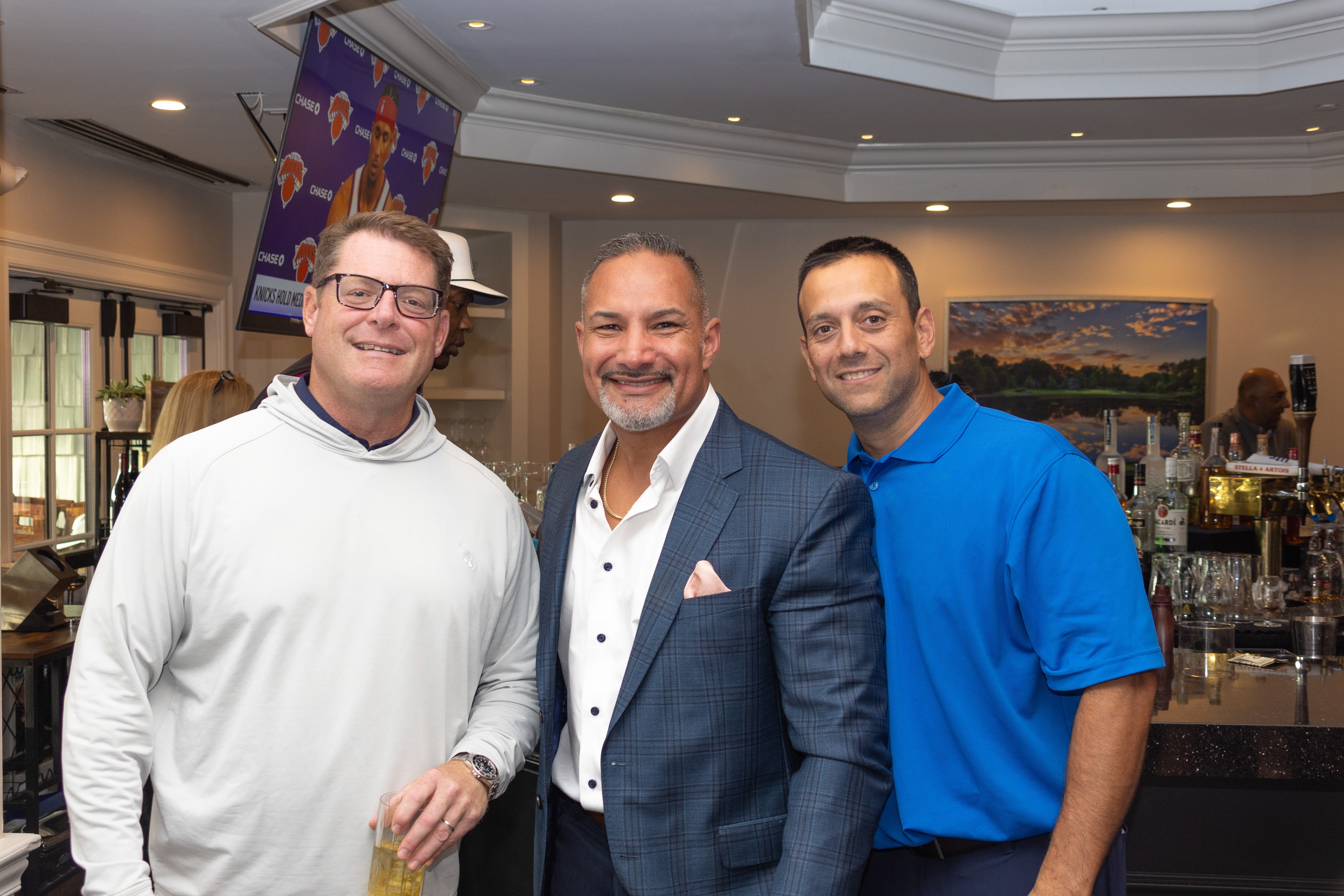 Three men pose for a photo near a cocktail bar