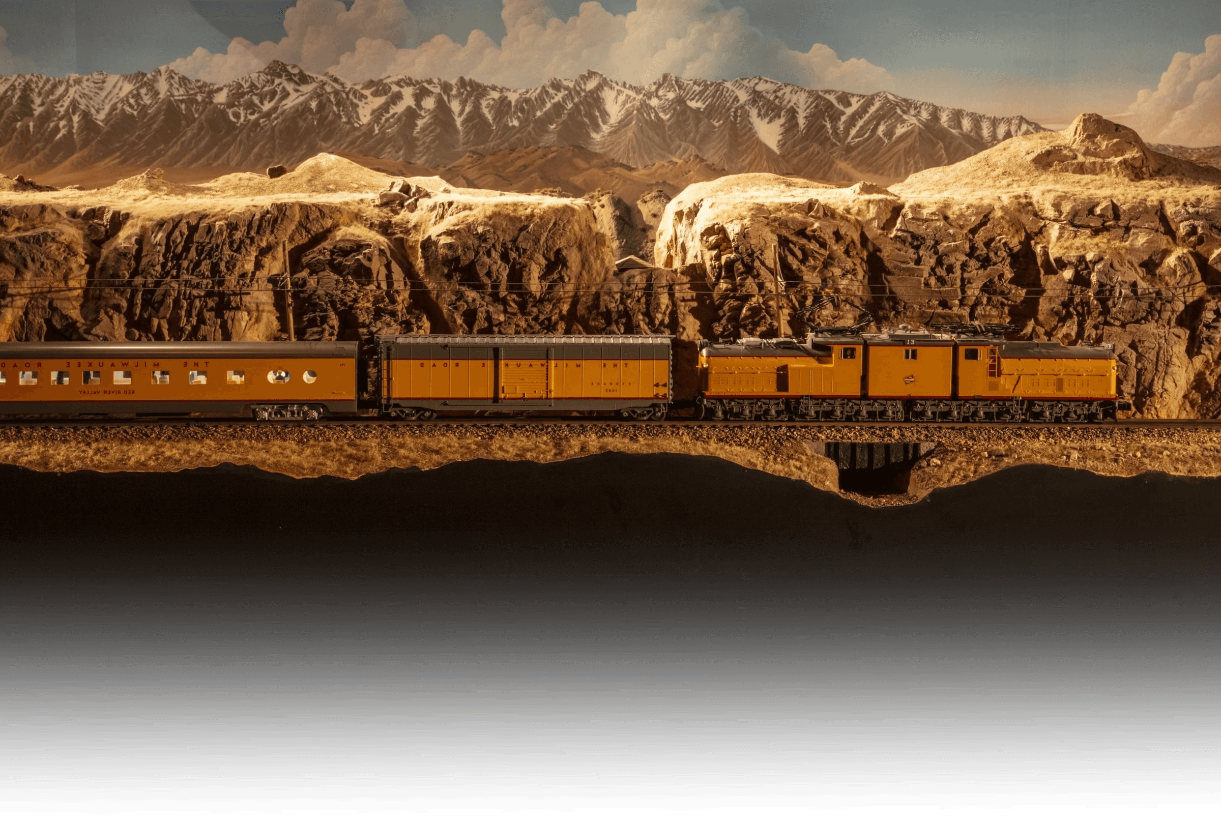 Orange Milwaukee Road electric train running beneath desert cliffs on the layout.