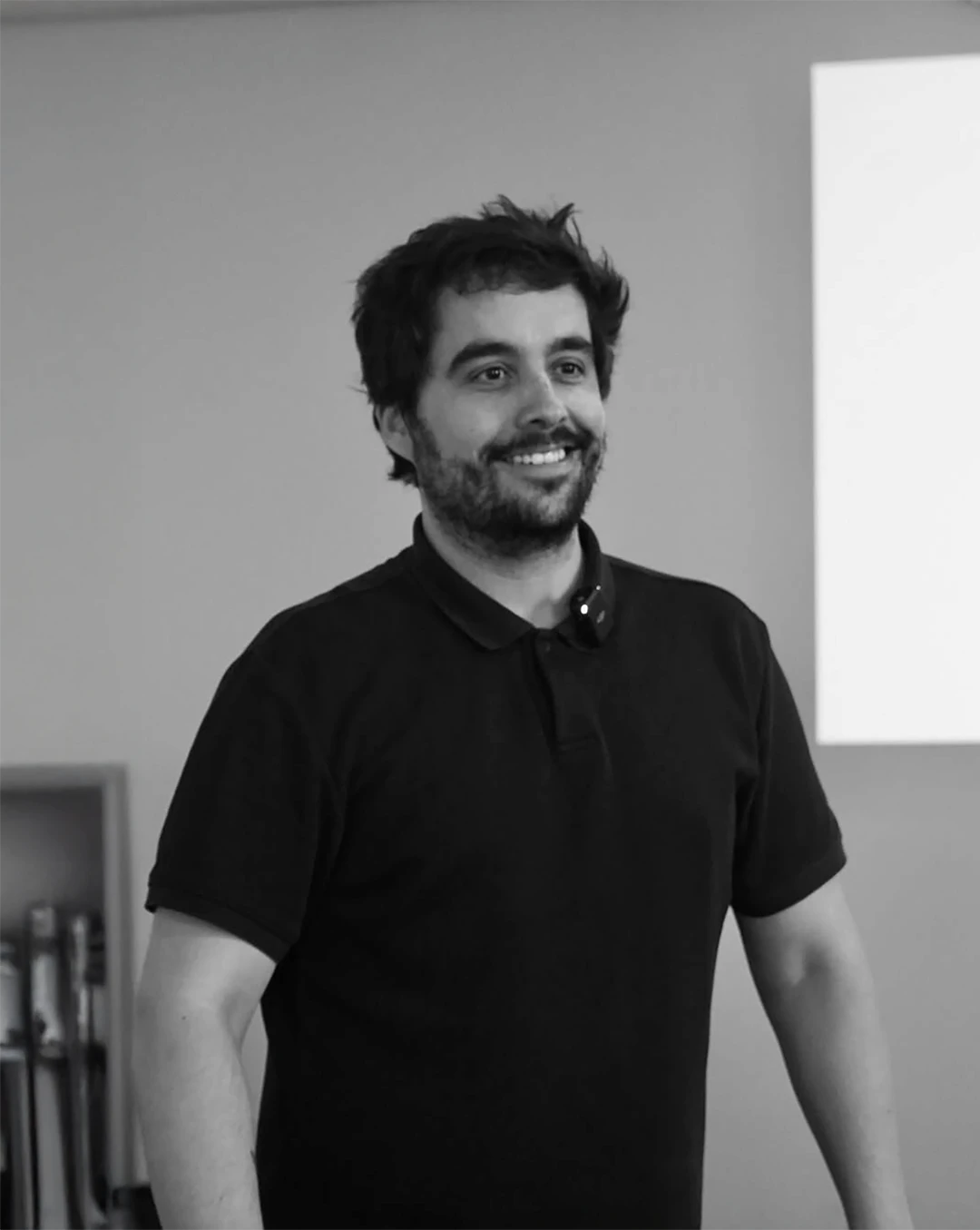 A smiling man in a suit and glasses sits at a table, with a modern office backdrop.