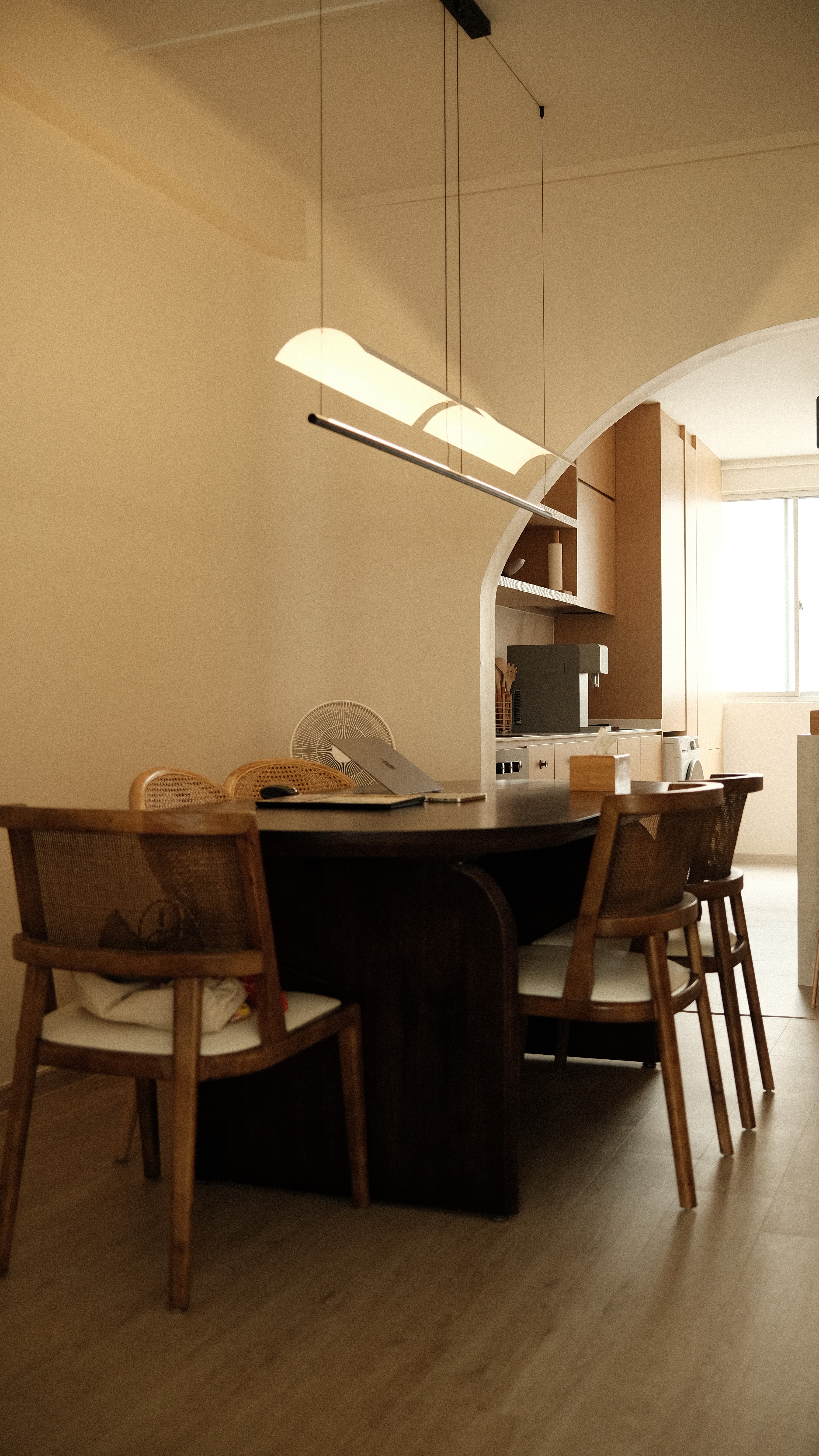 Contemporary dining area with dark wood table, rattan chairs, and arched opening, Singapore interior design