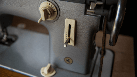 Close-up of vintage sewing machine controls showing stitch length and tension dials on a grey metal body.