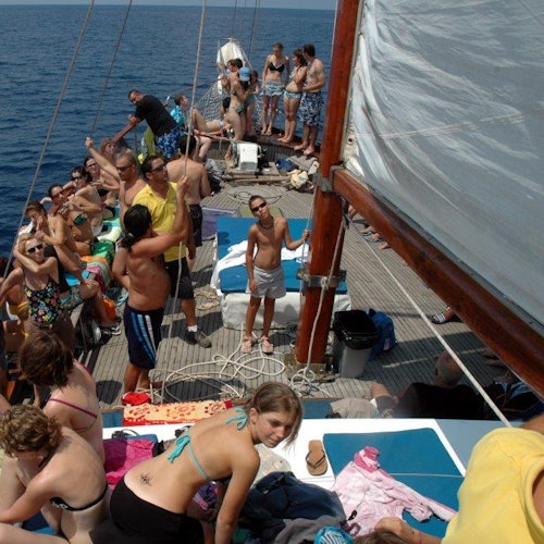A crowded sailboat with people in swimwear enjoying a sunny day on the open sea.