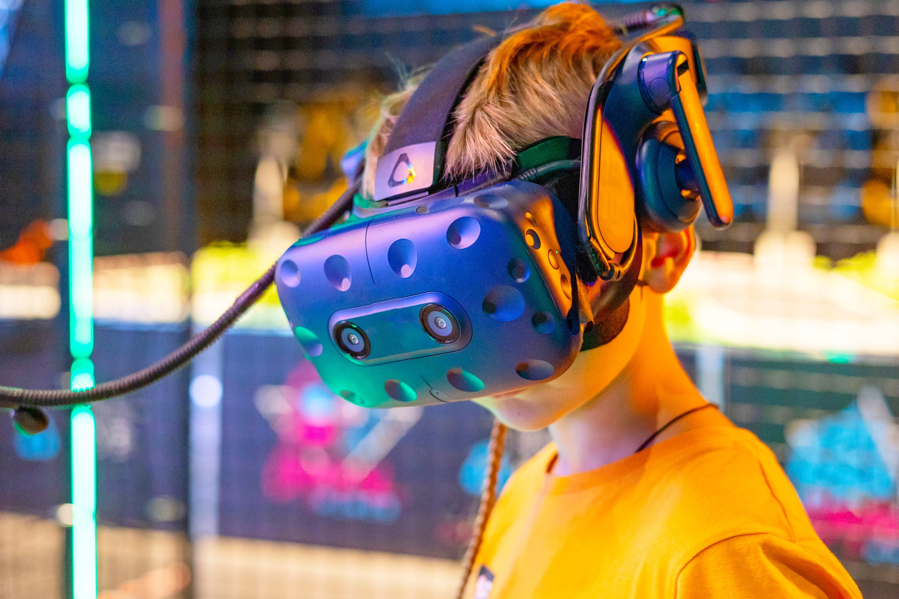 Young boy wearing a virtual reality headset and headphones immersed in a VR gaming experience, with neon-lit background.
