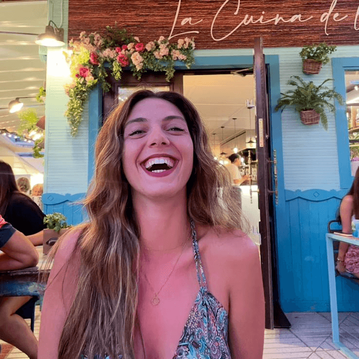 A woman in a white blouse and dark vest sits on a park bench, looking away and smiling. A ukulele rests next to her.