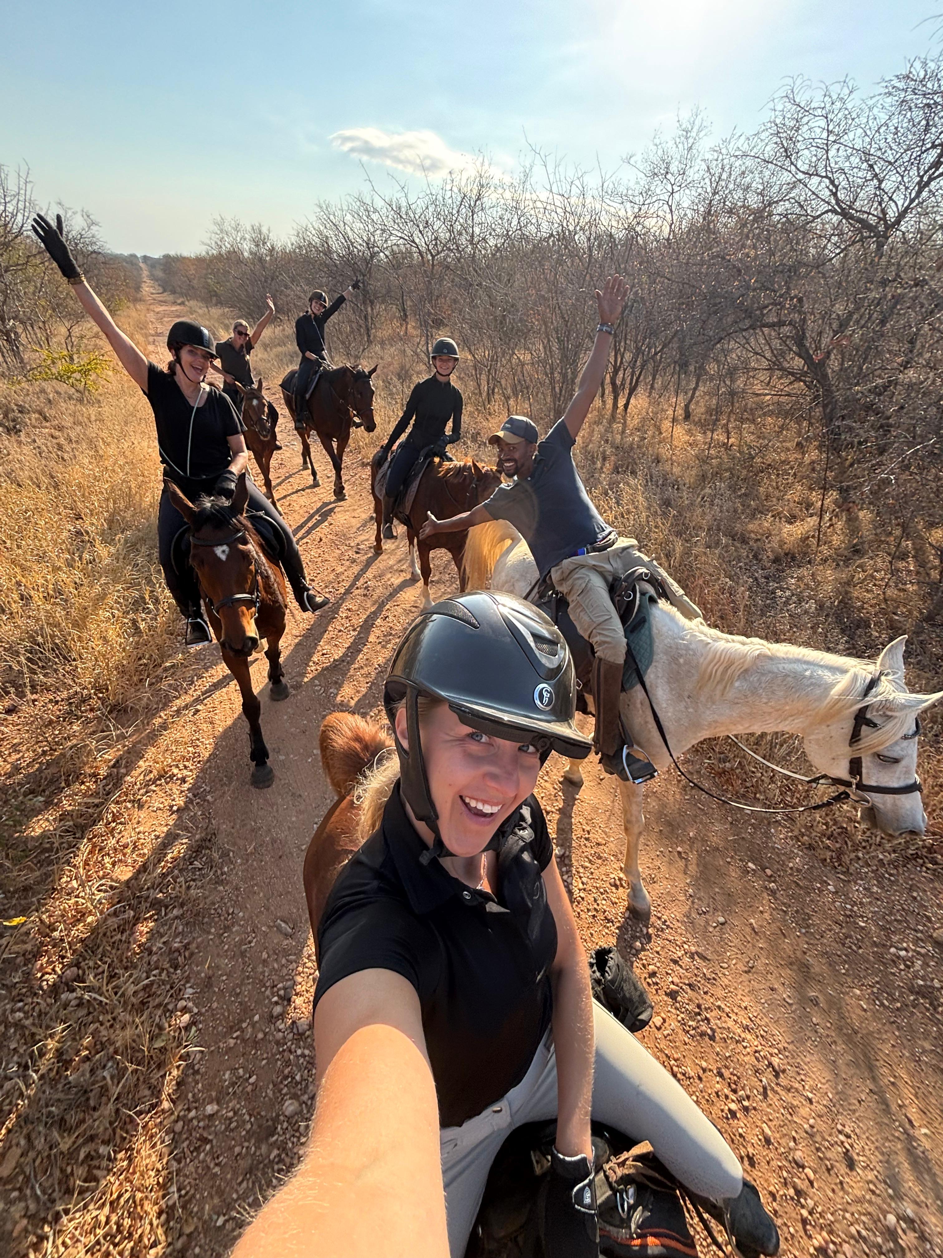 Kilimanjaro Elephant Ride, Arusha National Park, Tanzania – elefant i högt gräs tittar mot kameran, medan fem ryttare till häst på ridsafari i bakgrunden betraktar elefanten i ett grönt och frodigt landskap.