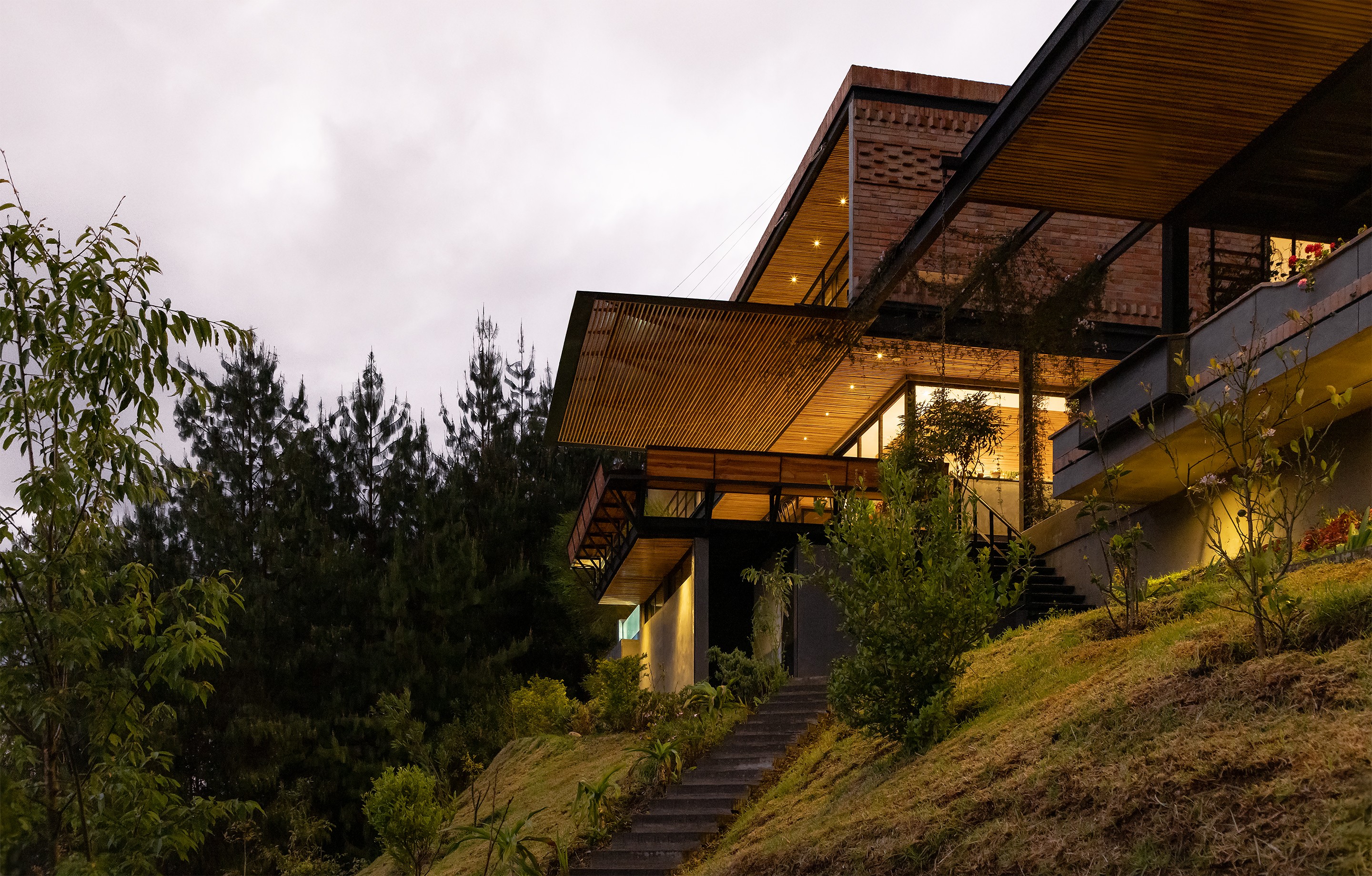 Perspectiva de casa moderna empotrada en la montaña con vista desde abajo con luces prendidas y voladizos y pérgolas