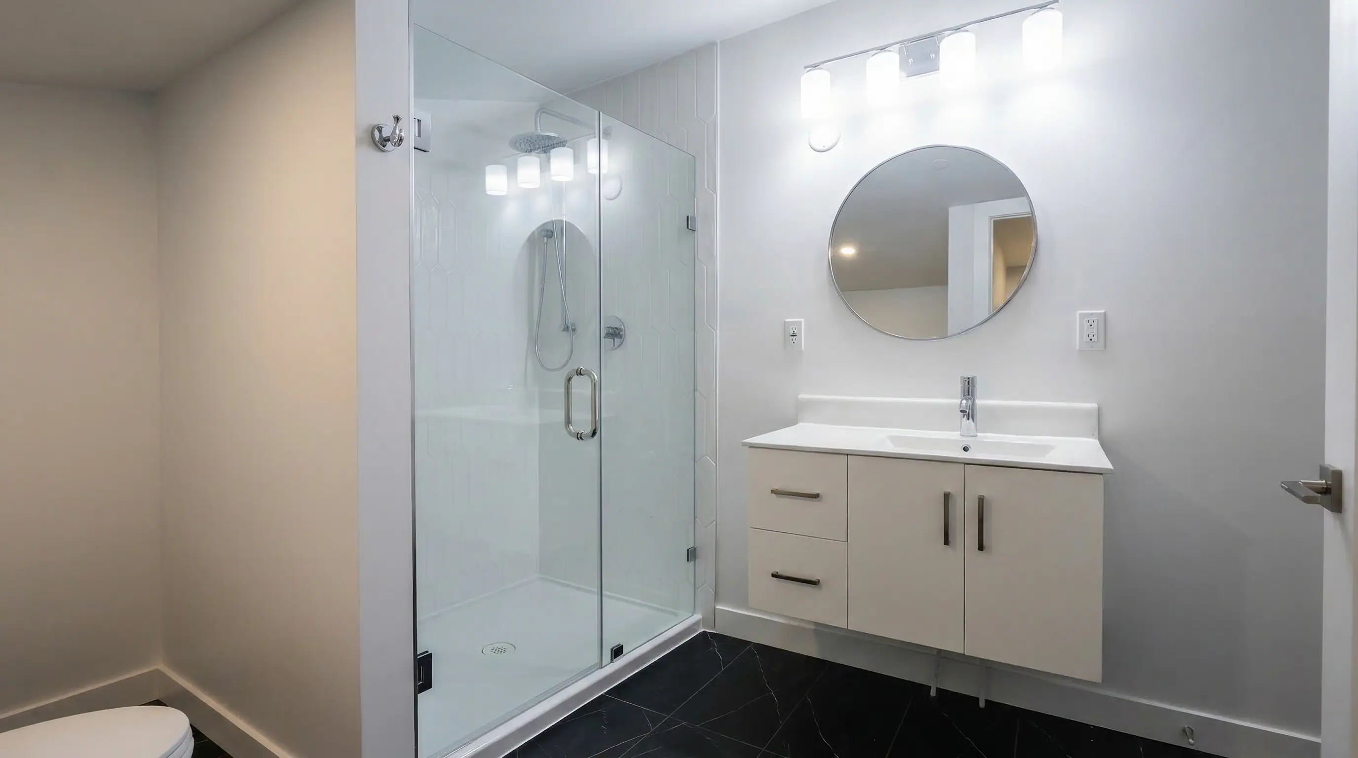 Modern ensuite bathroom in Vancouver Custom Homes' East 63rd laneway home with frameless glass walk-in shower, rain showerhead, floating vanity, and dark marble-look tile flooring.