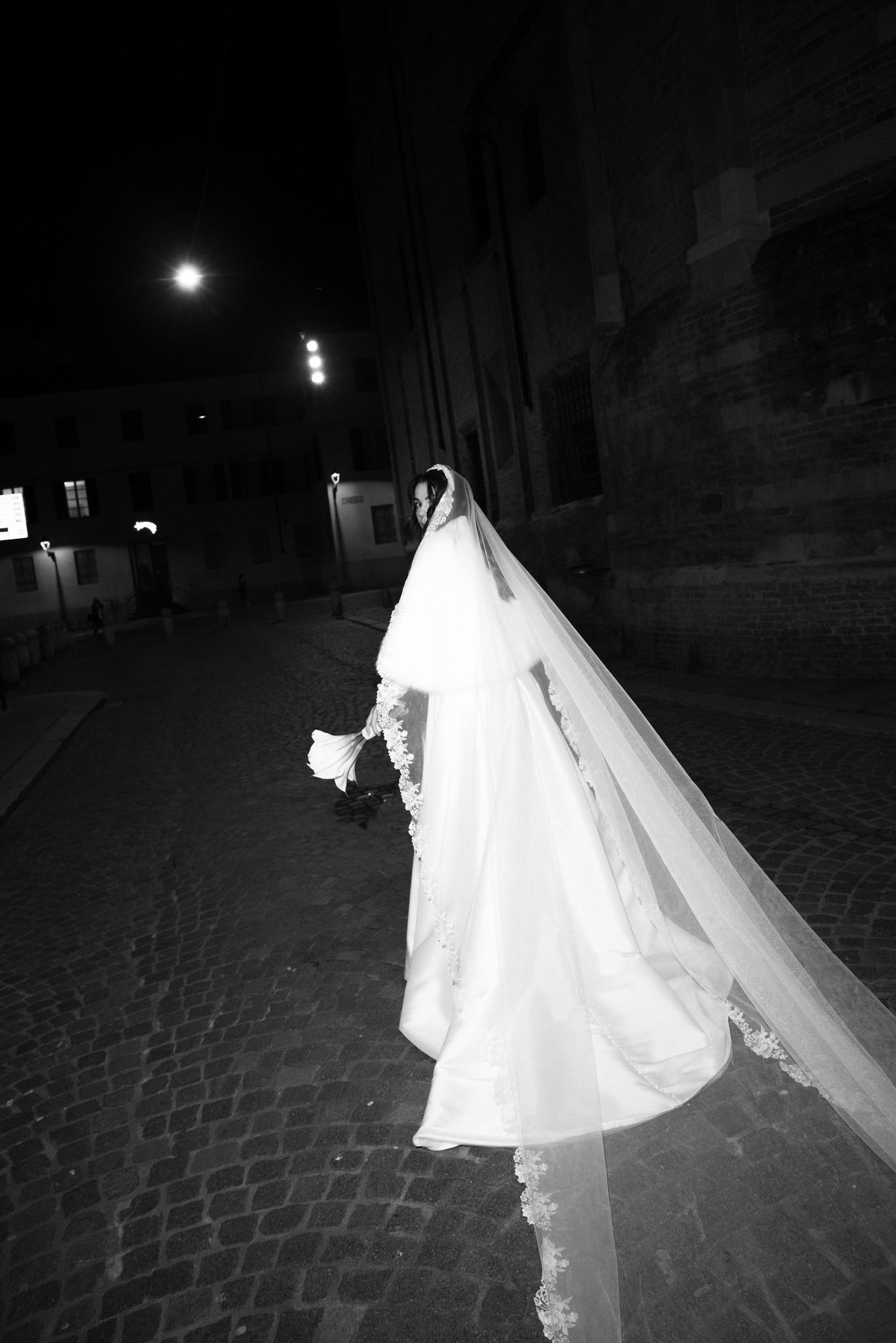 Sposa di spalle nel velo lungo cammina di notte al Circolo di Lettura a Parma, reportage matrimoniale in bianco e nero