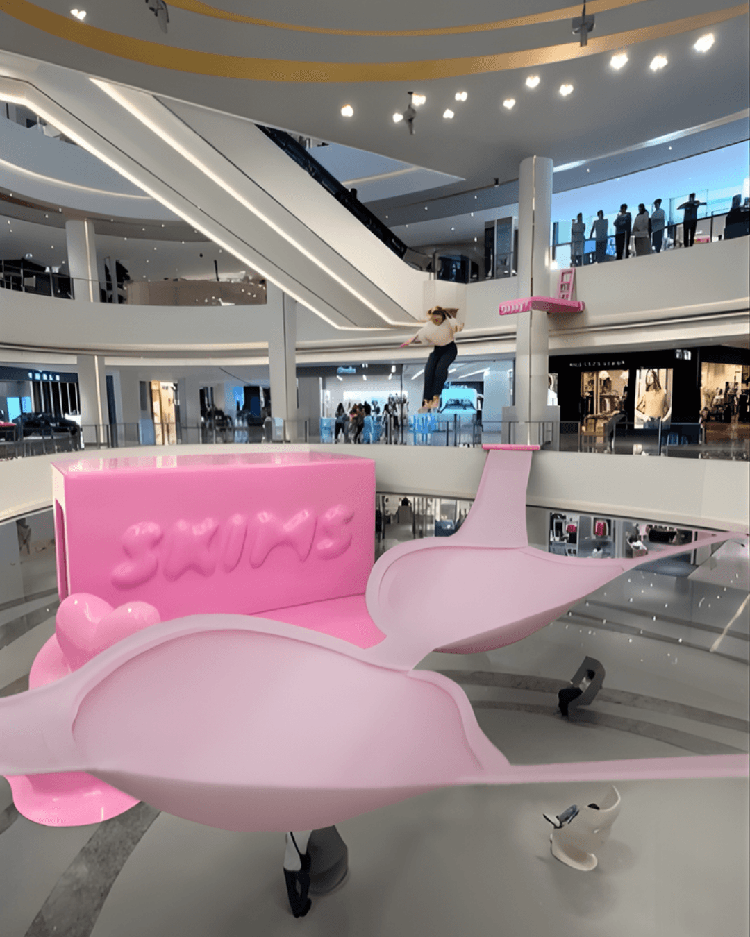 A final composited shot shows a person jumping from a pink platform onto the giant SKIMS inflatable bra
