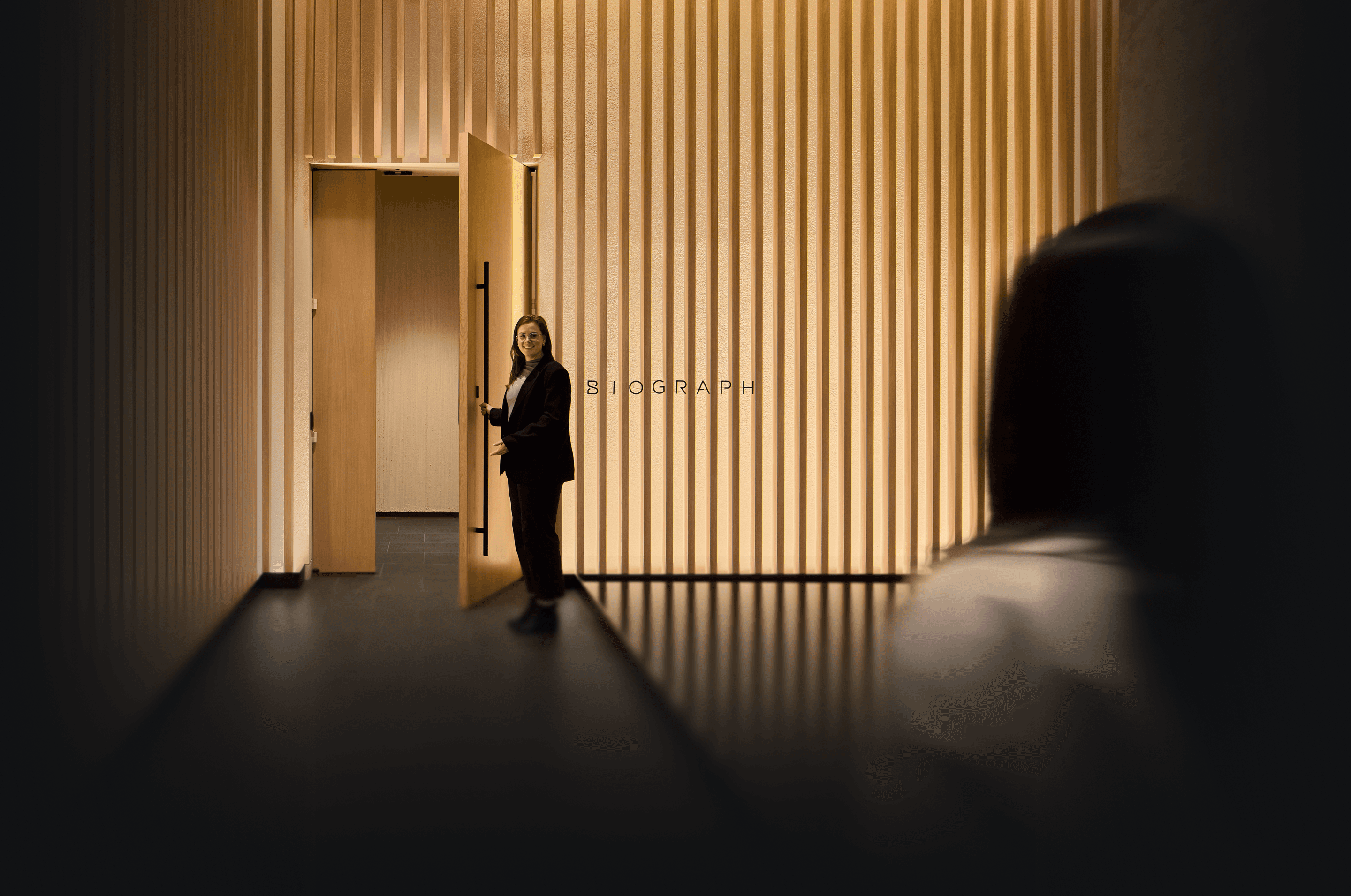 Biograph Clinic San Mateo exterior at night, featuring a glass pavilion with vertical wood slats, warm interior lighting, and minimalist architectural design.