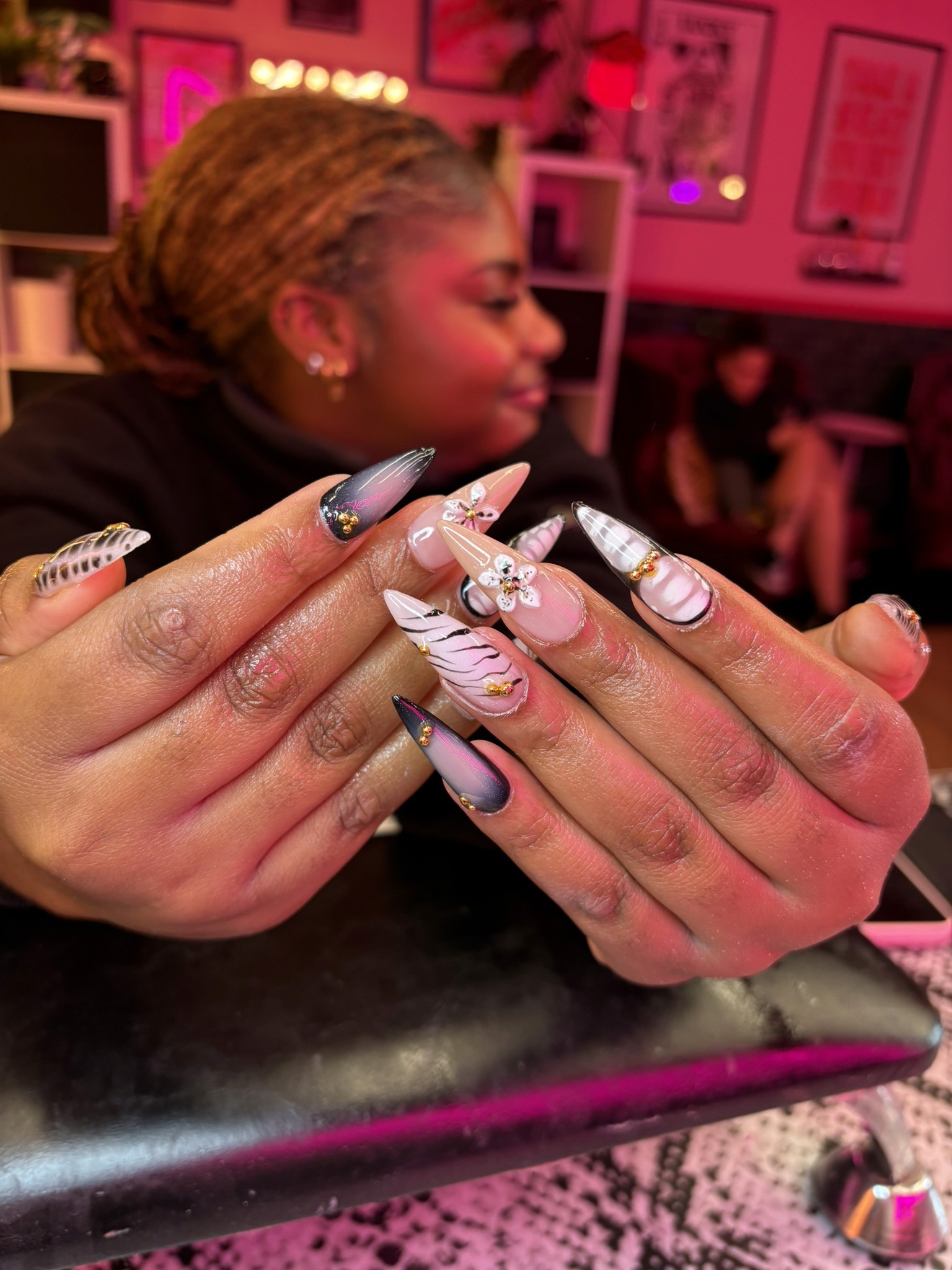 Long stiletto nails featuring a mix of grey-to-black gradients, hand-painted white 3D flowers with gold centers, and delicate black-and-white grid patterns.