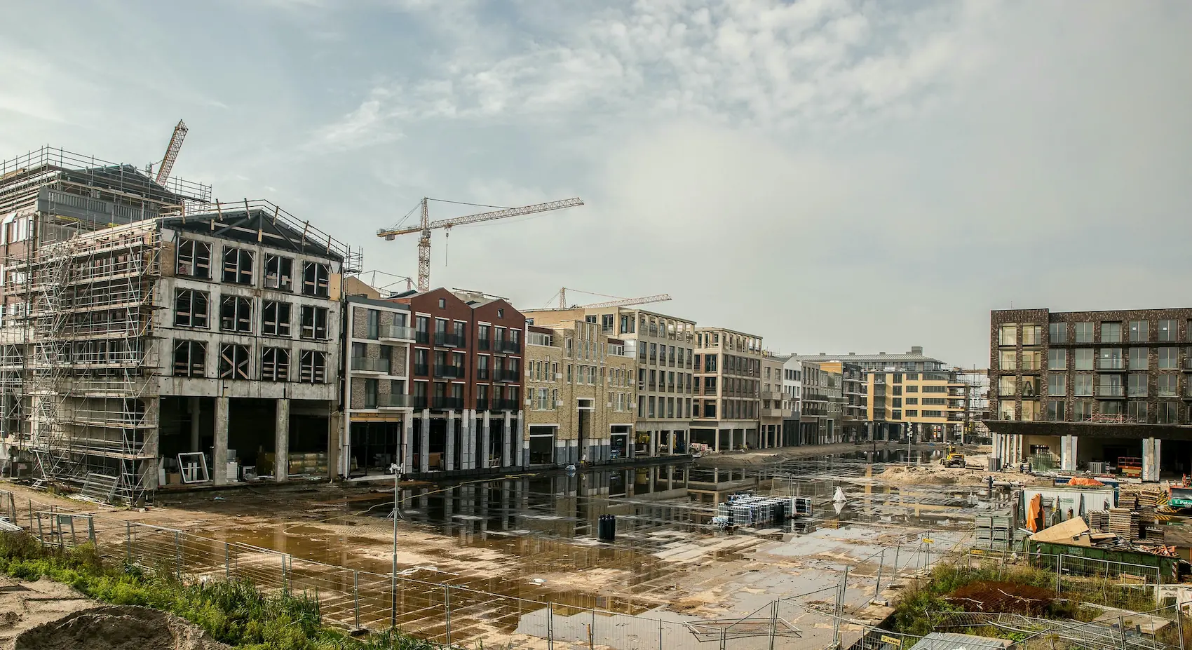 Wide view of a residential development construction site featuring unfinished brick buildings and tower cranes
