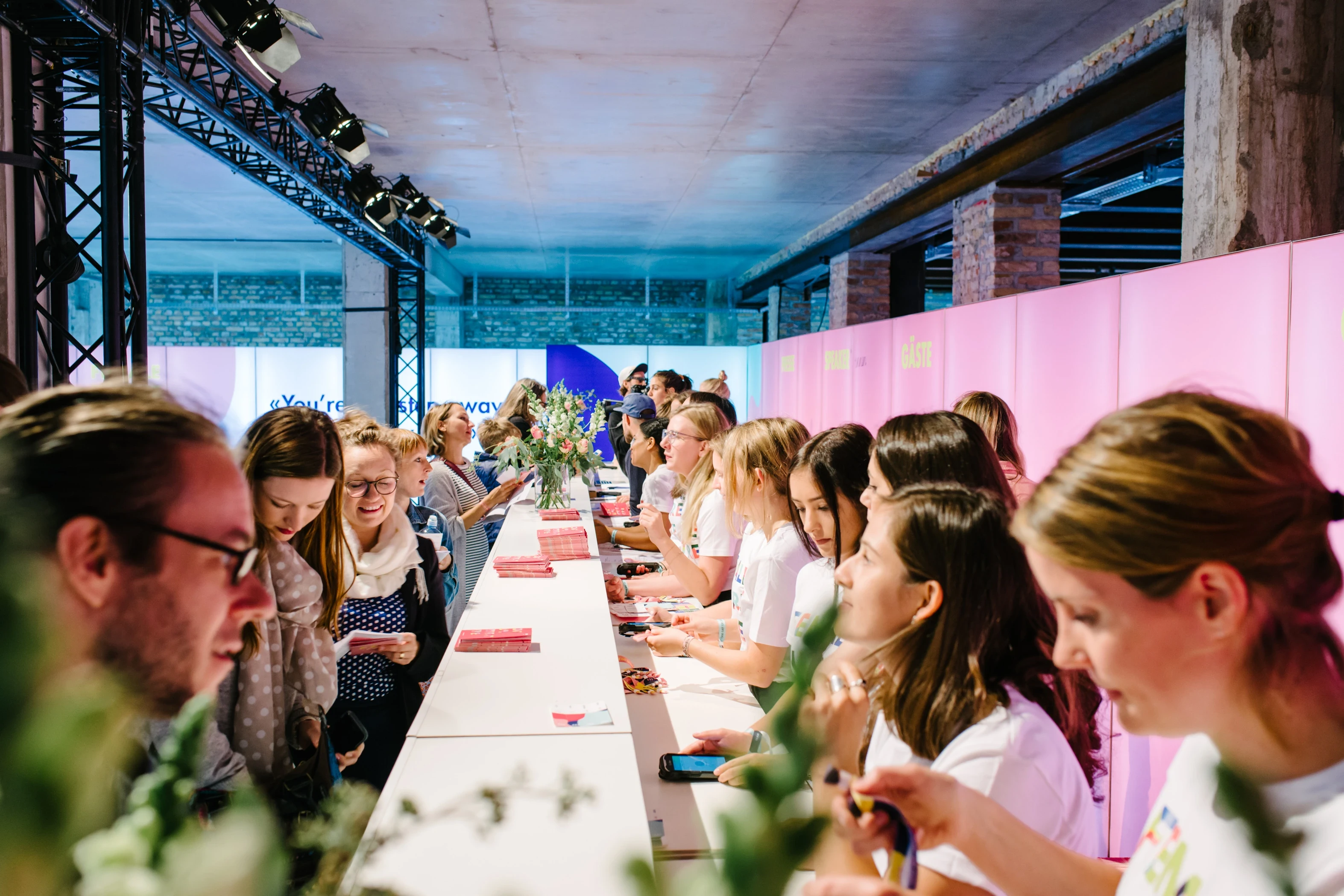 Long white registration counter at the FEMALE FUTURE FORCE DAY with staff handing out red badges to a queue of visitors.