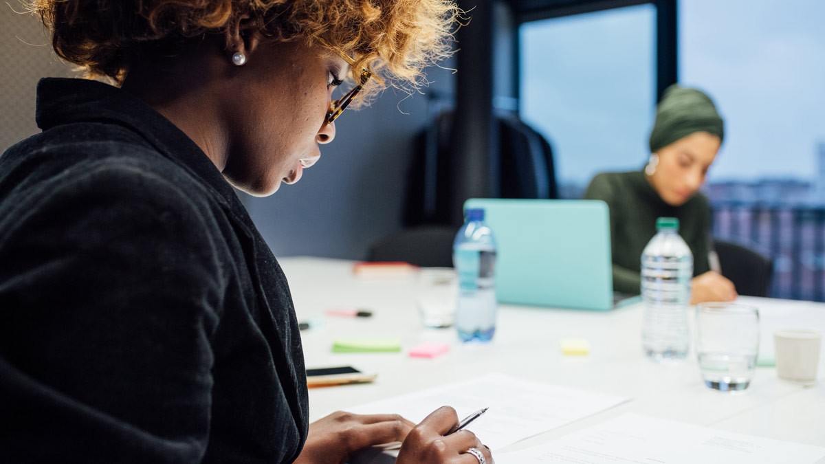 Two co-workers sitting around a conference table and taking notes during a meeting