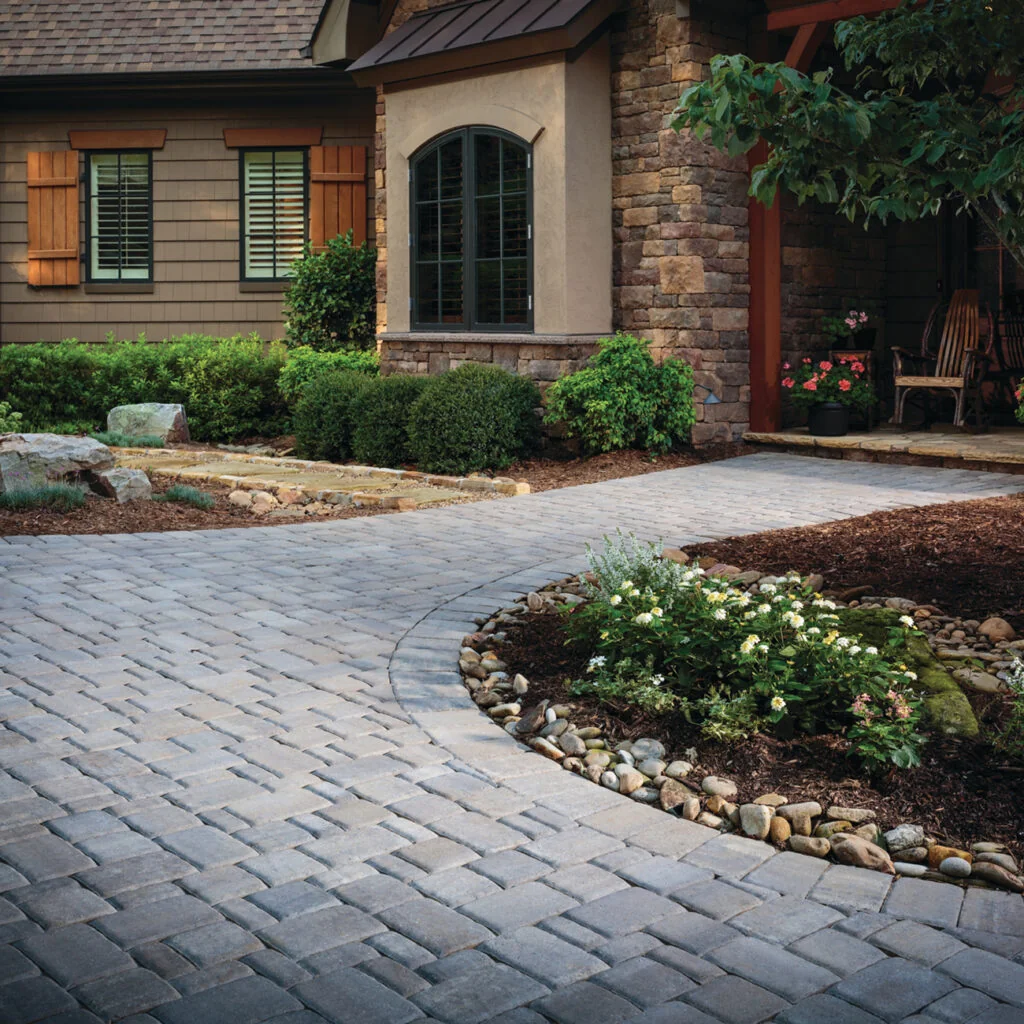 Gray paver walkway curving around a planted bed toward a stone and wood front porch.