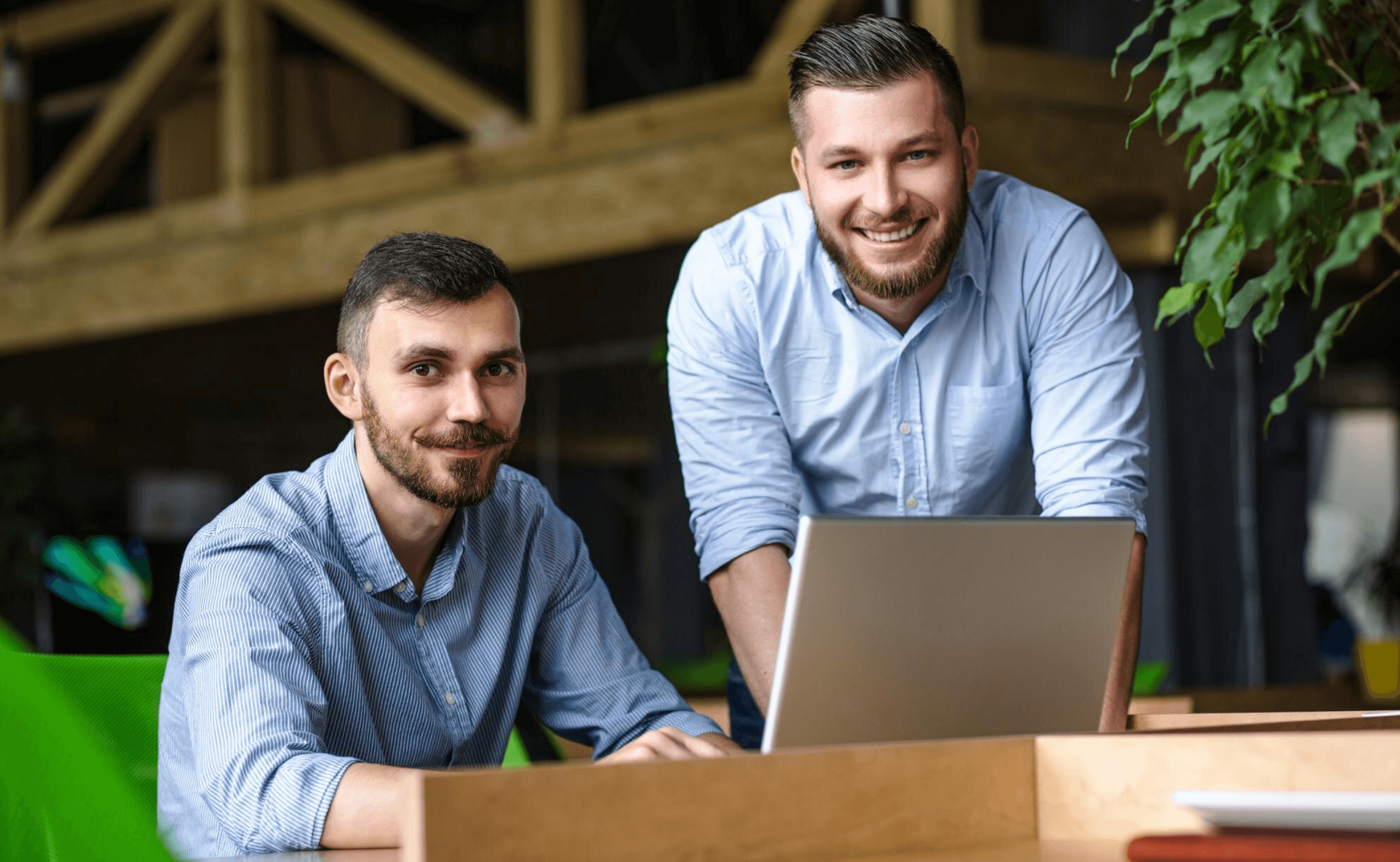 Two people smiling near a laptop in a modern office with wood and plants