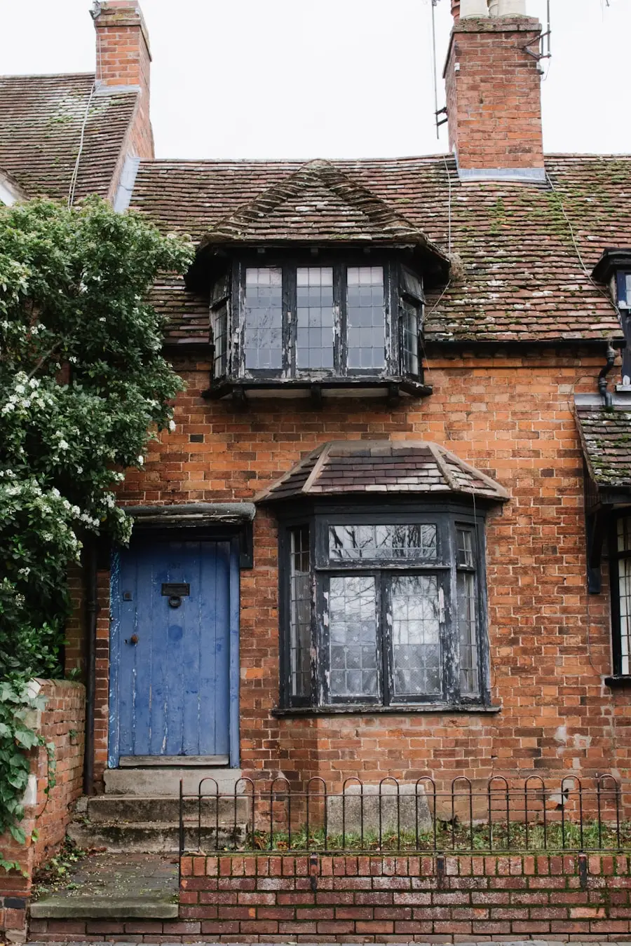 A dark brick house with a projecting bay window and a painted front door