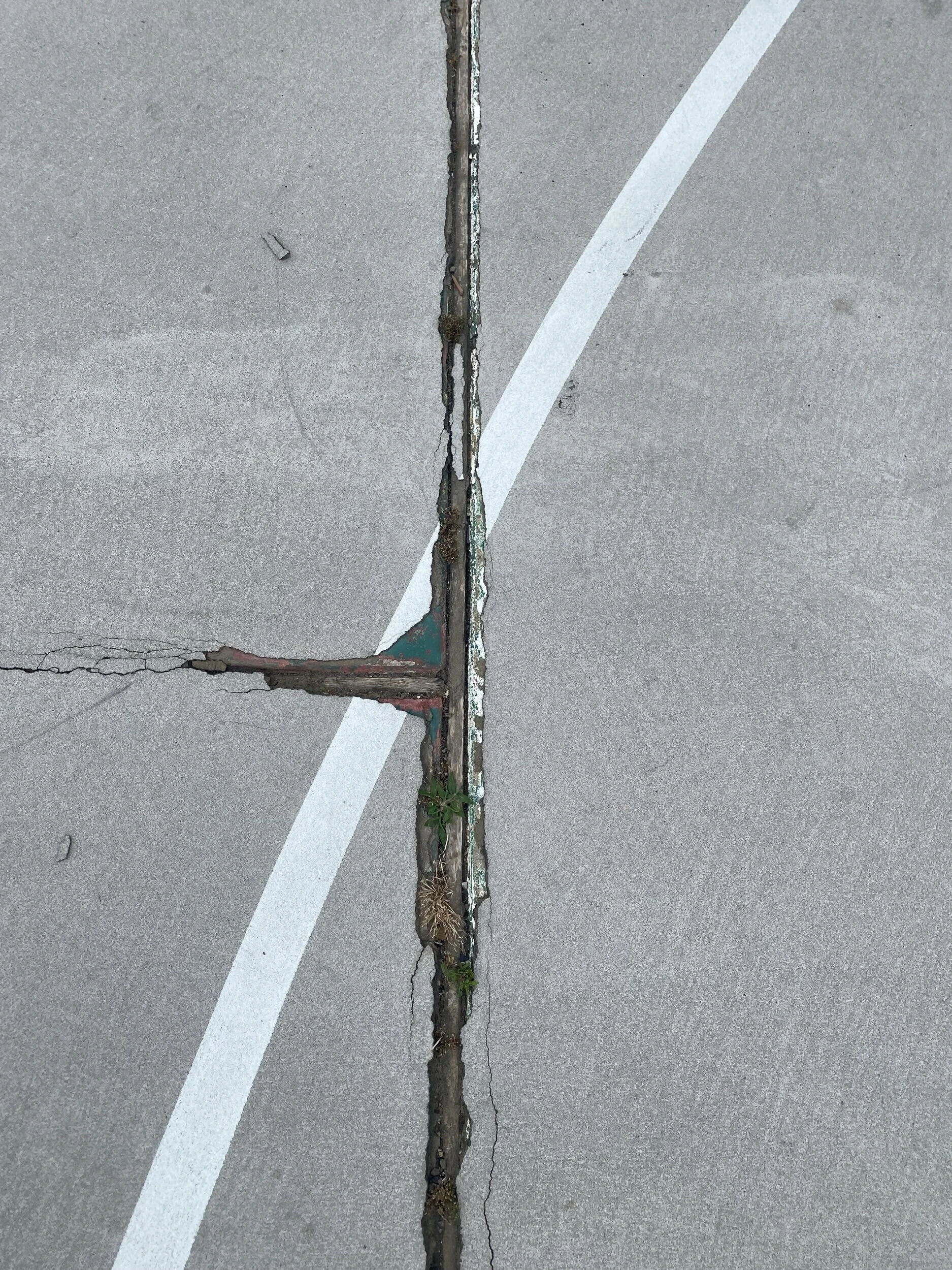 Cracked expansion joint with old patch material on court surface before resurfacing at Bell Park in Greenwood, AR