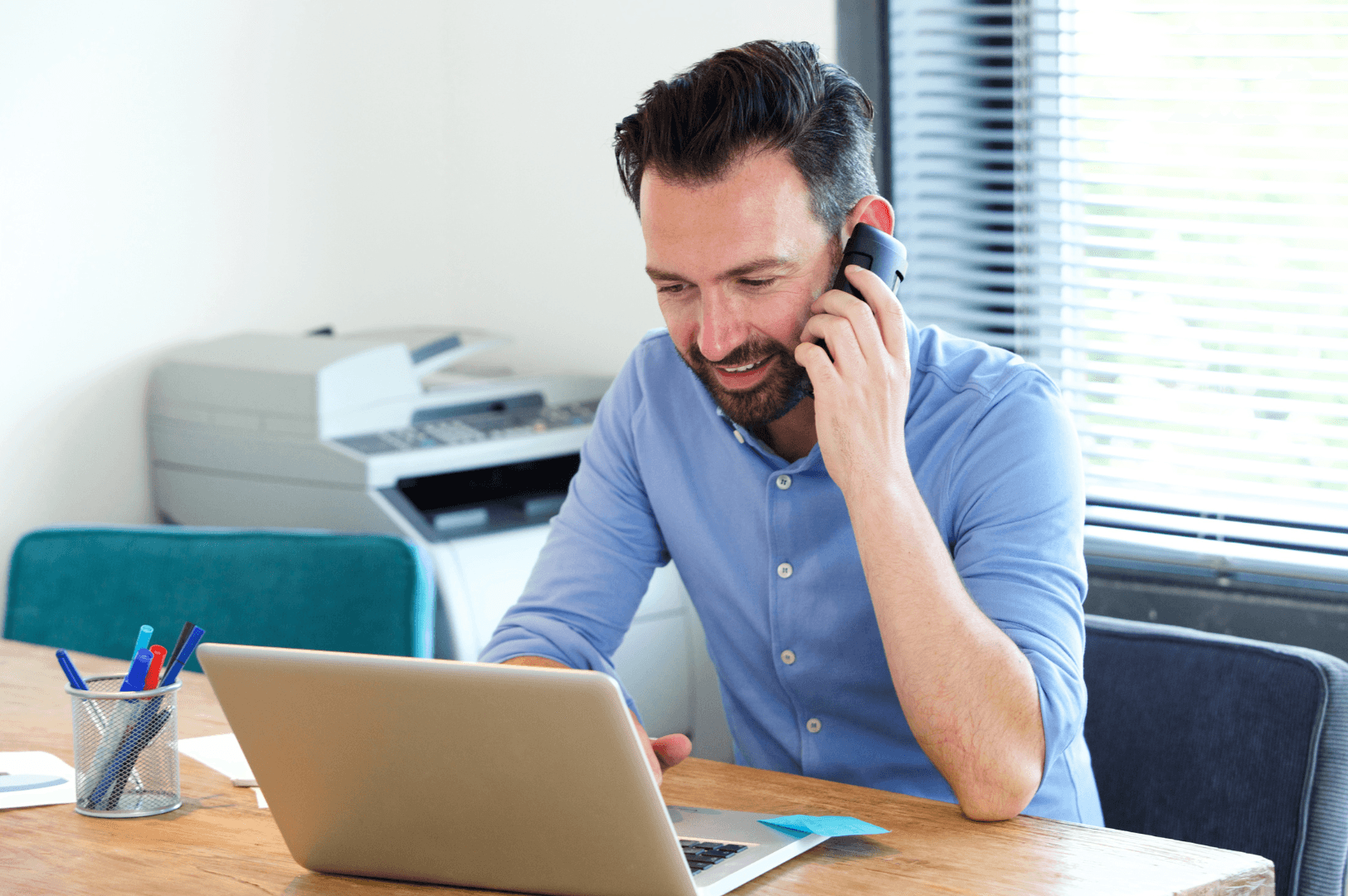 Smiley man talking on the phone while looking at laptop screen