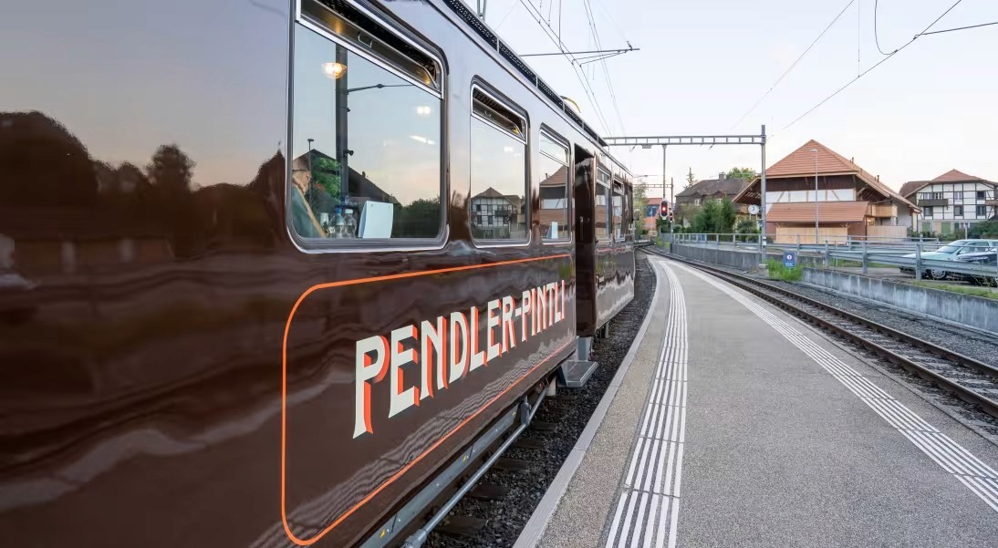 Der braune historische Zug Pendler Pintli an einem Bahnhofperron.