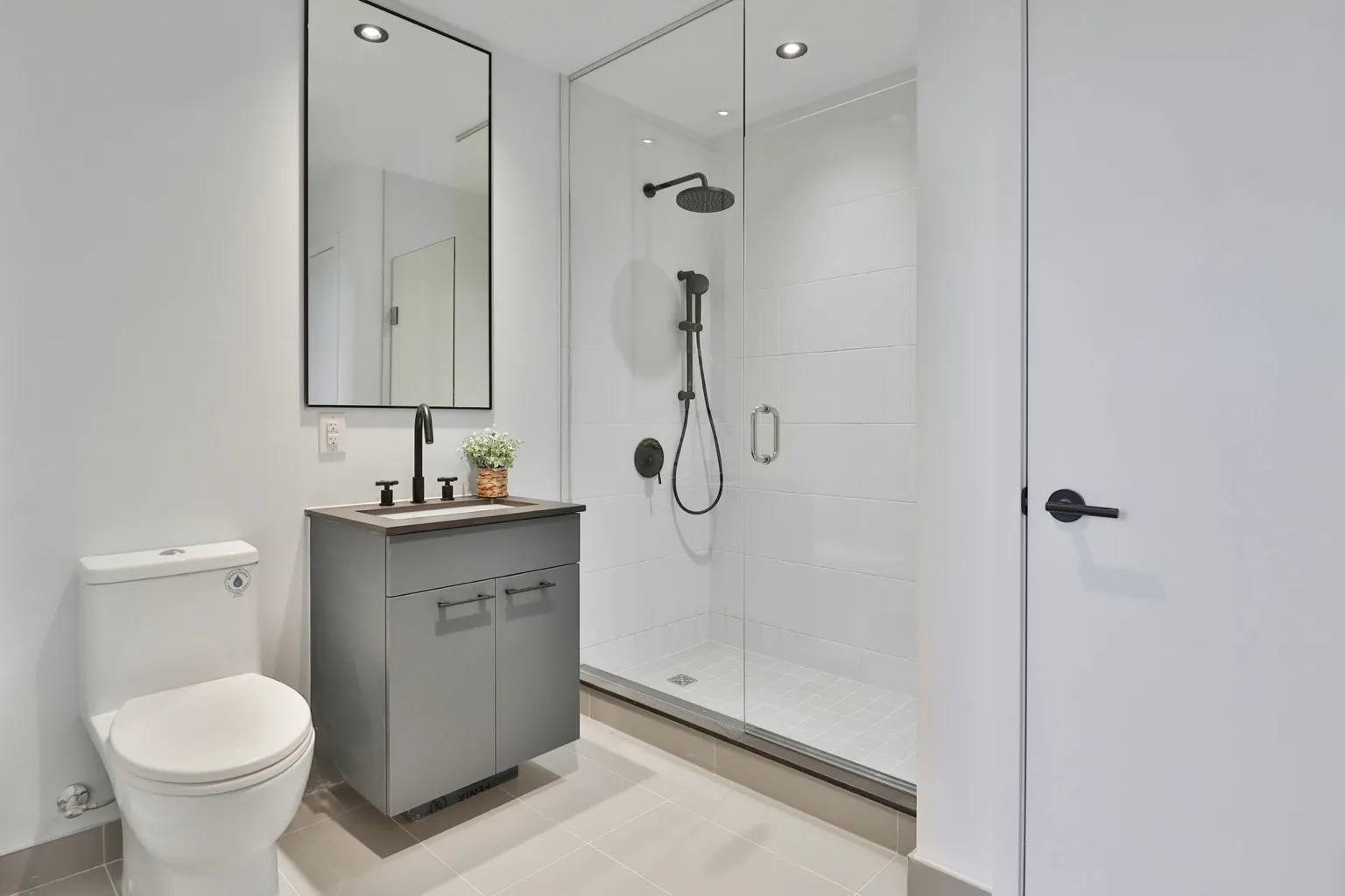 Bagno moderno con lavabo grigio, specchio grande rettangolare, doccia con parete in vetro e sanitari bianchi.