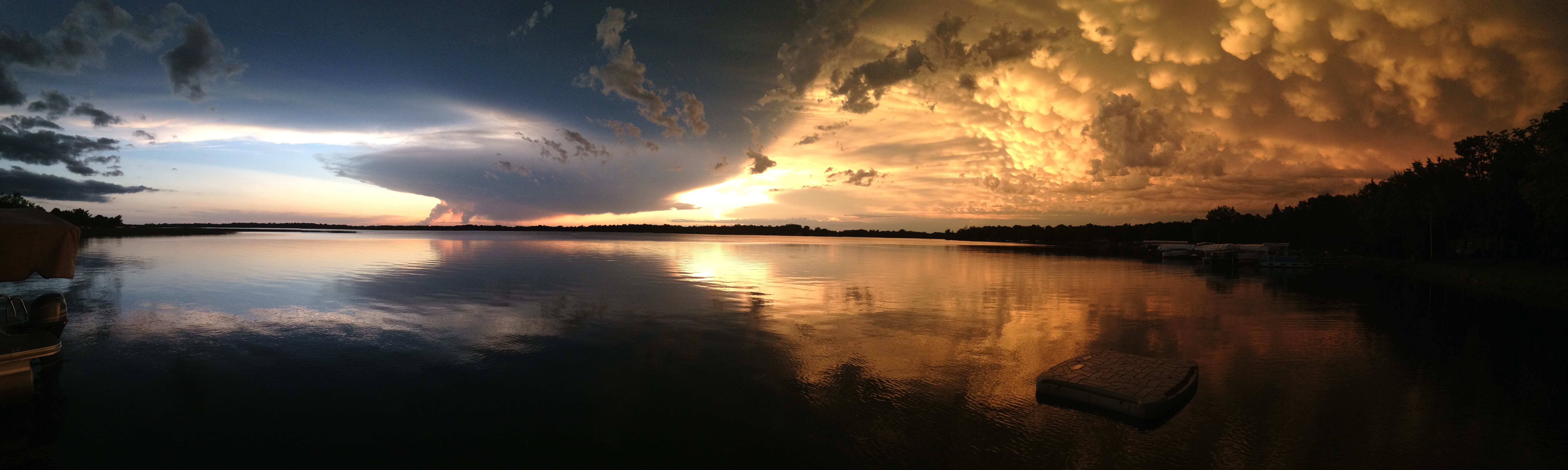 Panoramic view of a lake beneath dramatic clouds and warm evening light.