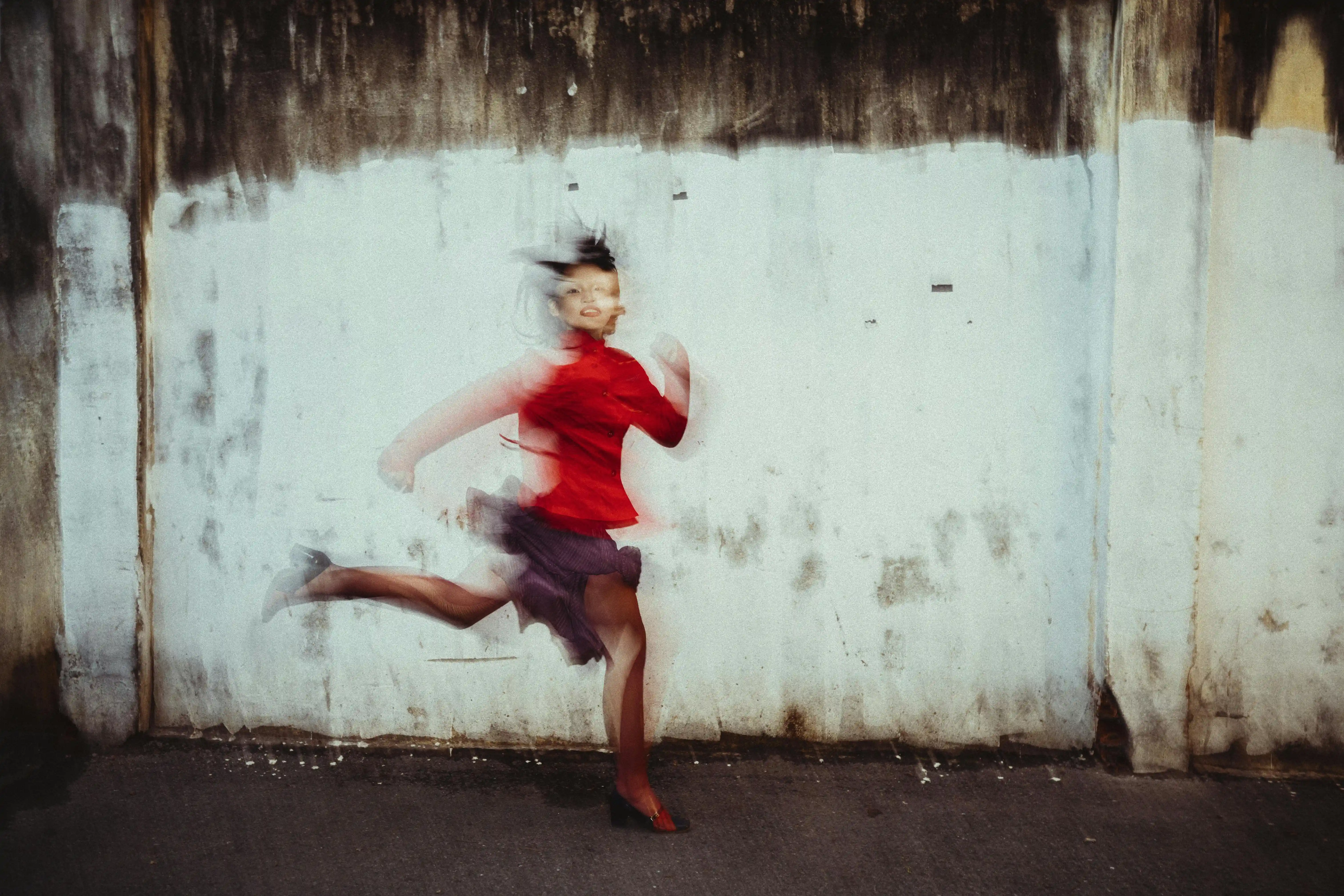 Aesthetically blured image of a woman wearing bright red shirt running along concrete wall.