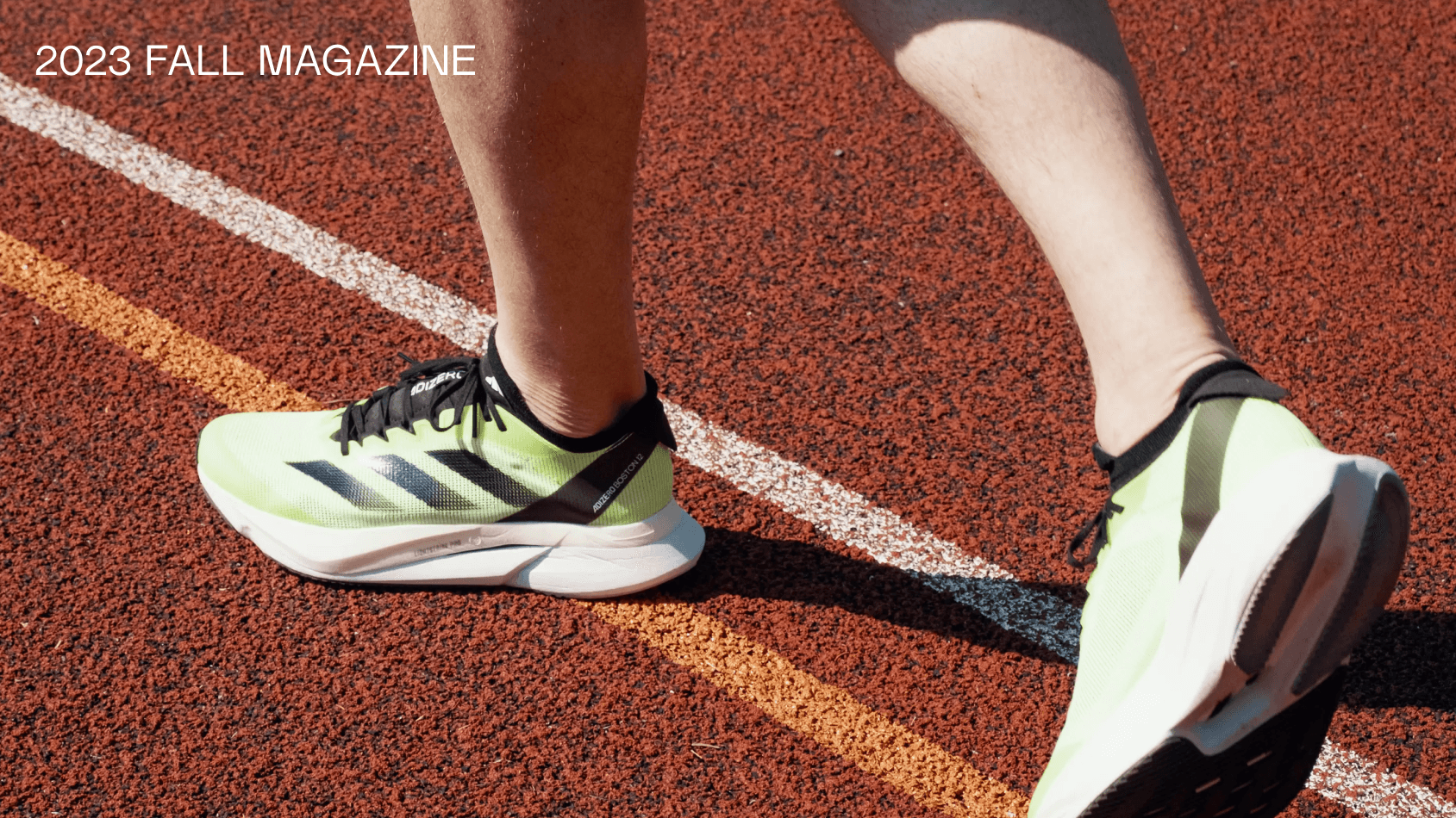 Closeup of a persons two feet ready to start running. Wearing green sneakers on a trackfield. There is also the text Fall magazine on the image. 