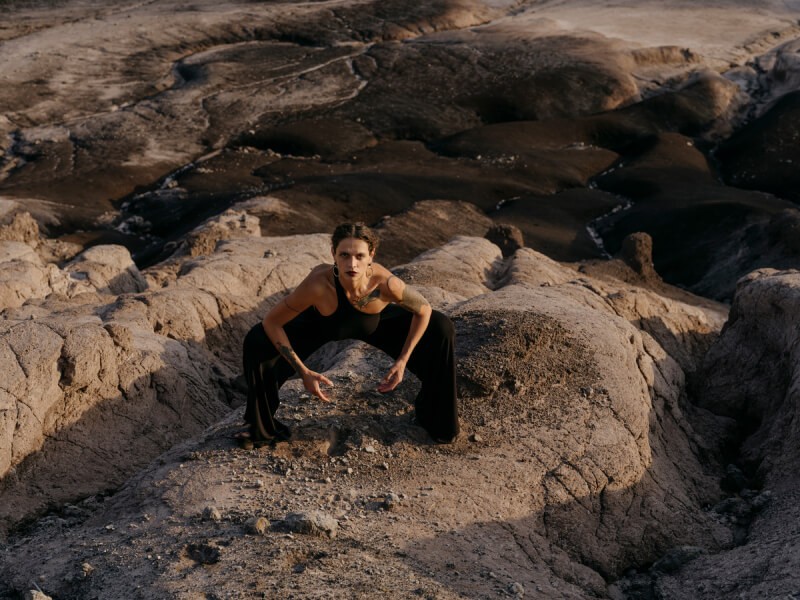 Blertë Dibrani frontal in hockender Pose auf einem Felsen